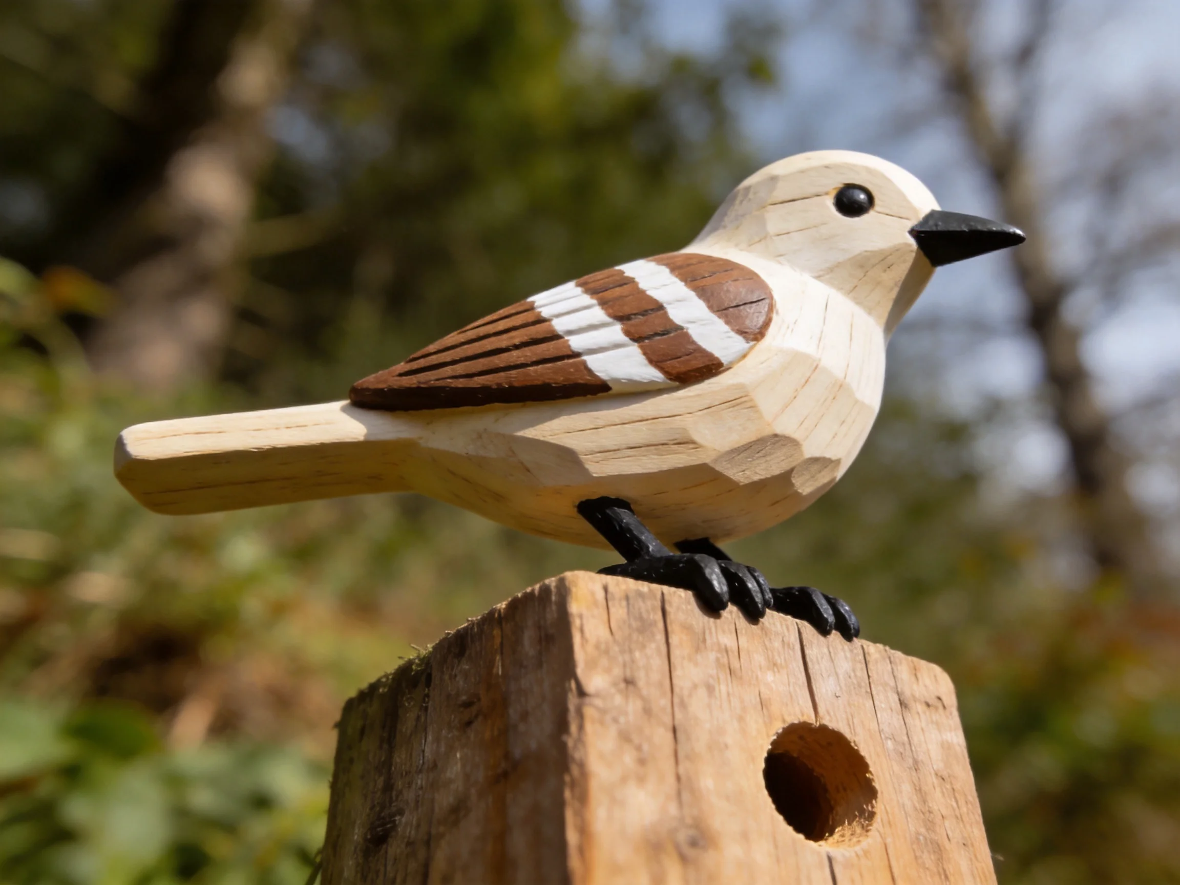 A handcrafted wooden bird figurine with brown and white wing markings perches on a wooden post