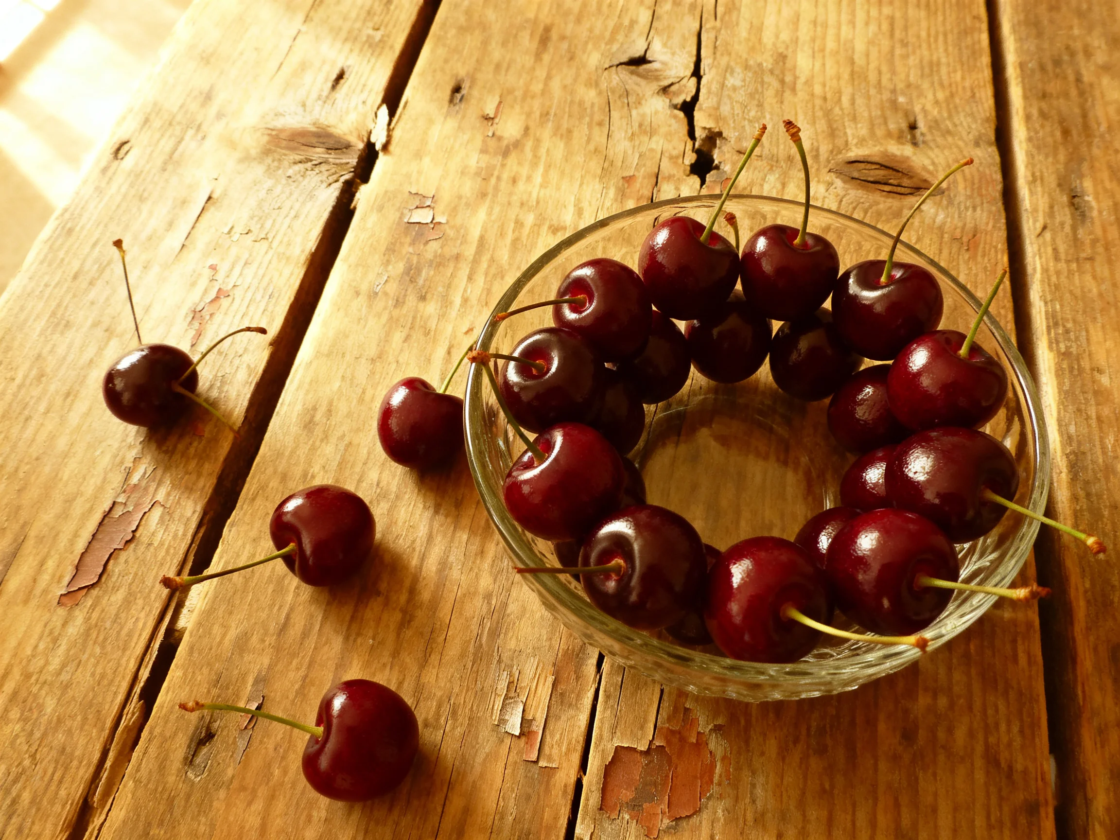 Dark cherries arranged in a glass bowl on a weathered wooden table