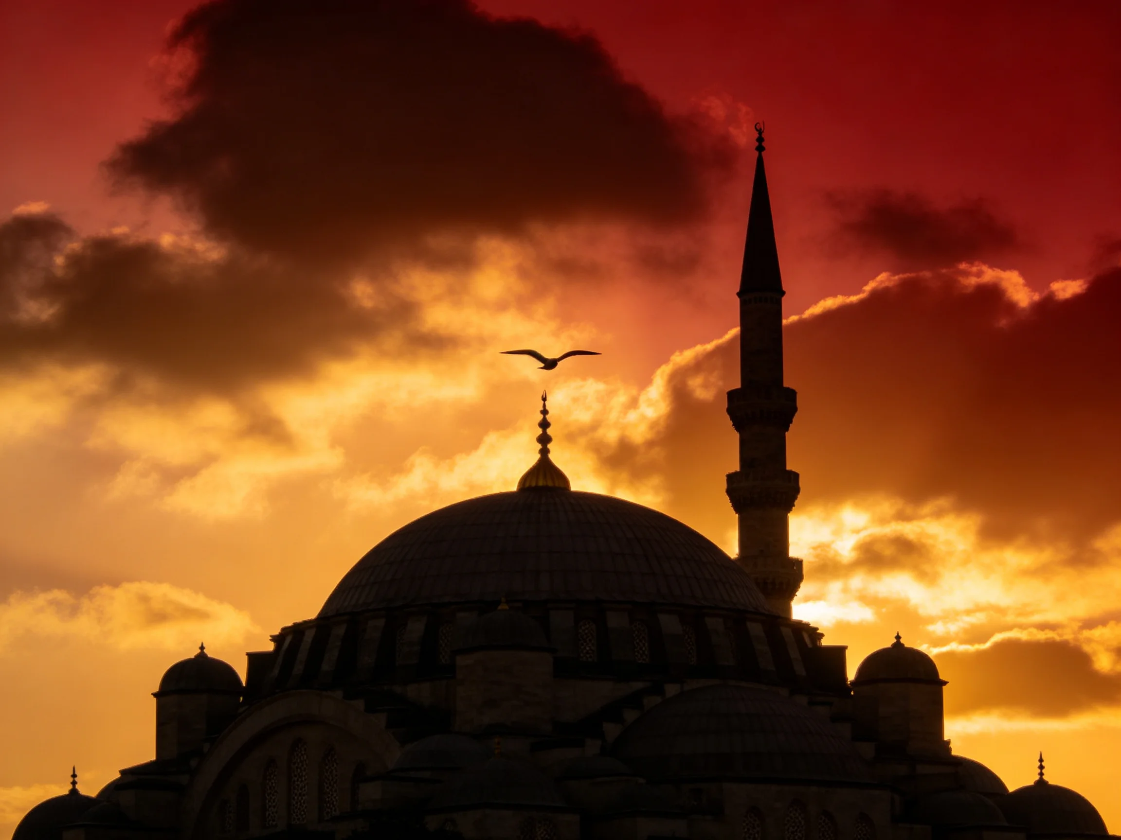 Silhouetted mosque with minaret against fiery sunset sky