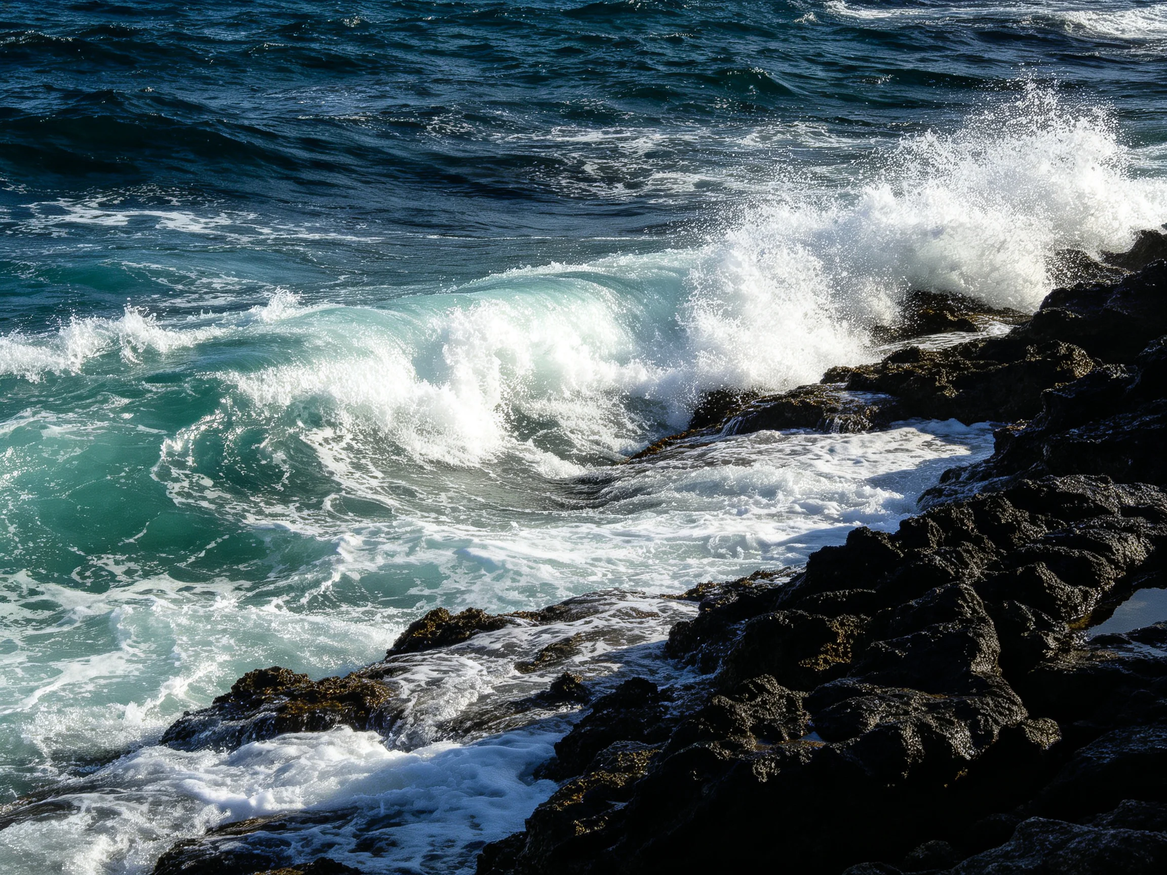 Turquoise waves crash against dark jagged rocks by the shore