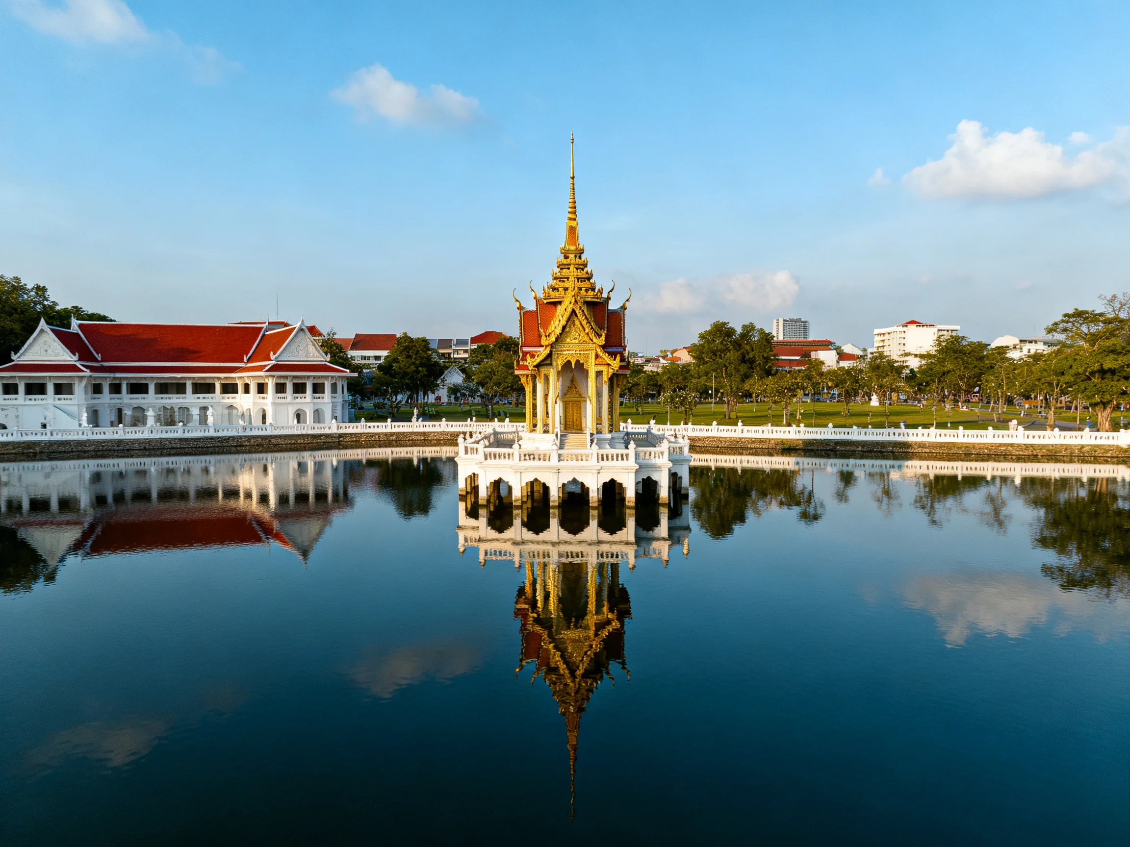 A Golden Pavilion Reflects in Blue Water Near White Buildings