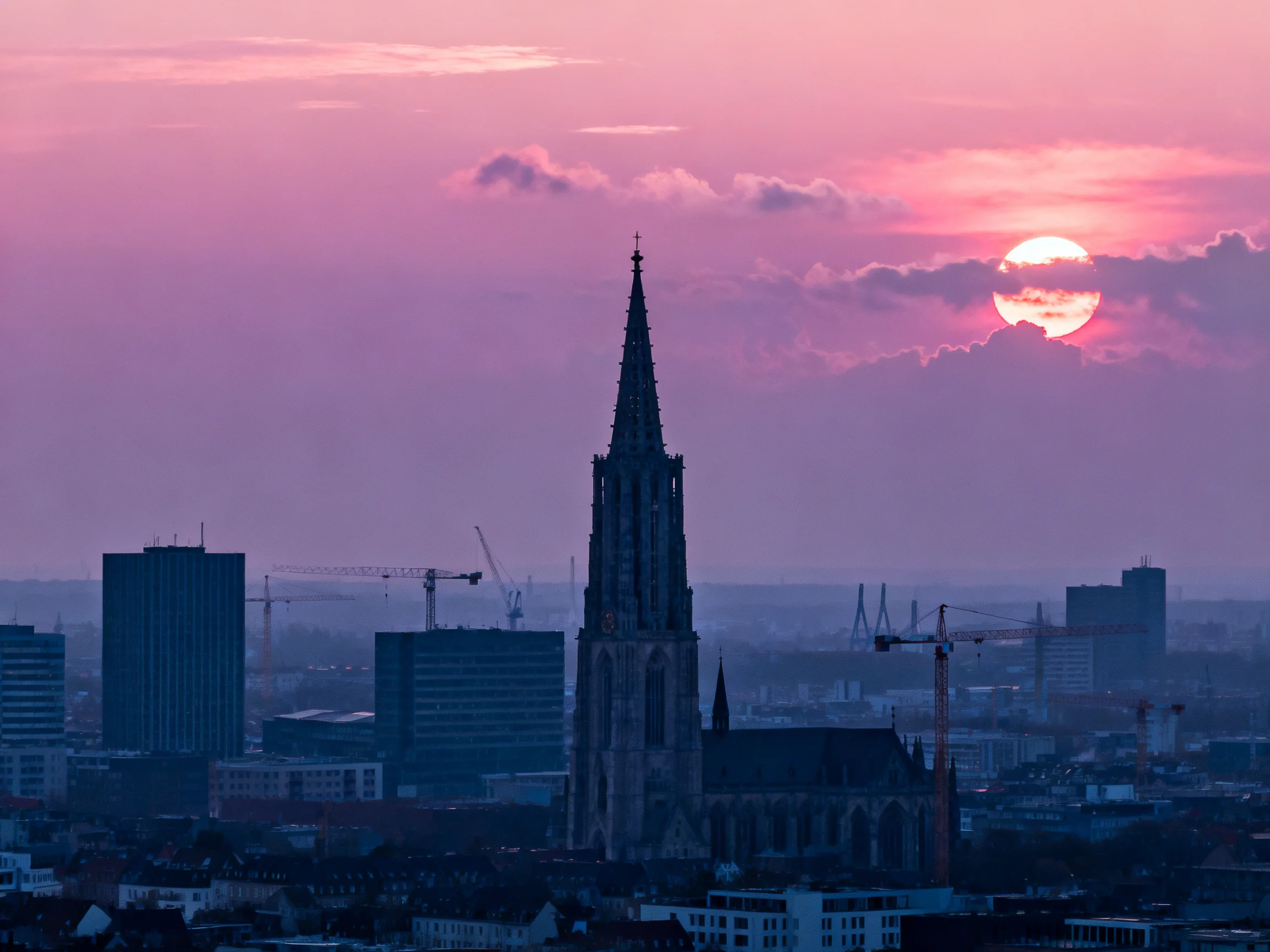 A Gothic Church Tower Beneath a Pink-Hued Urban Sunset Sky