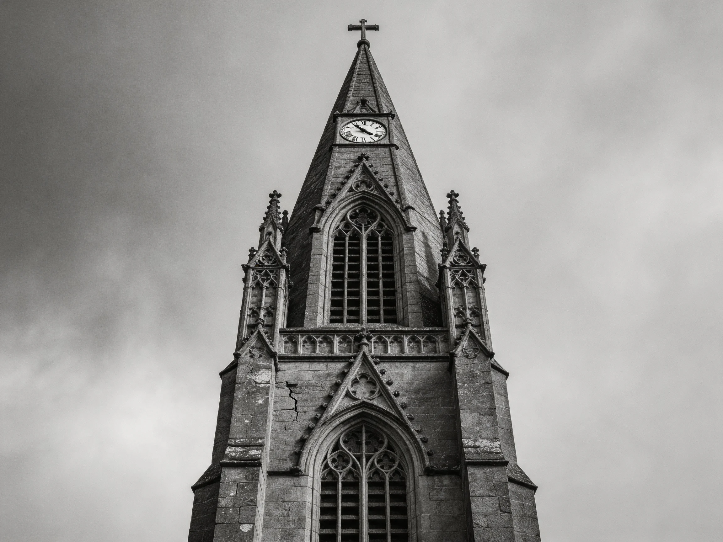 A Gothic church tower withclock and cross against a cloudy sky