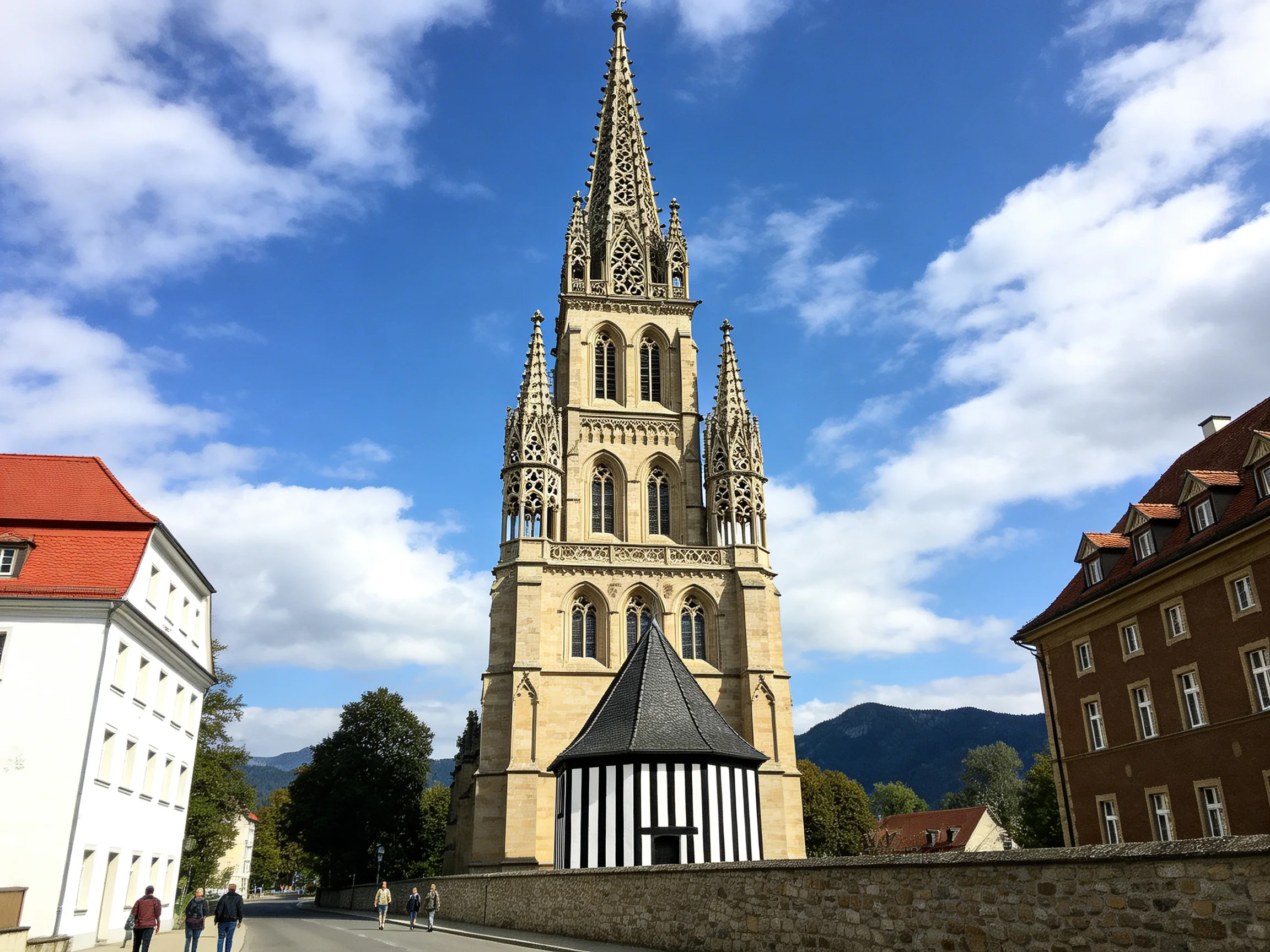 A Gothic tower with ornate spires near historic buildings under a bright blue sky