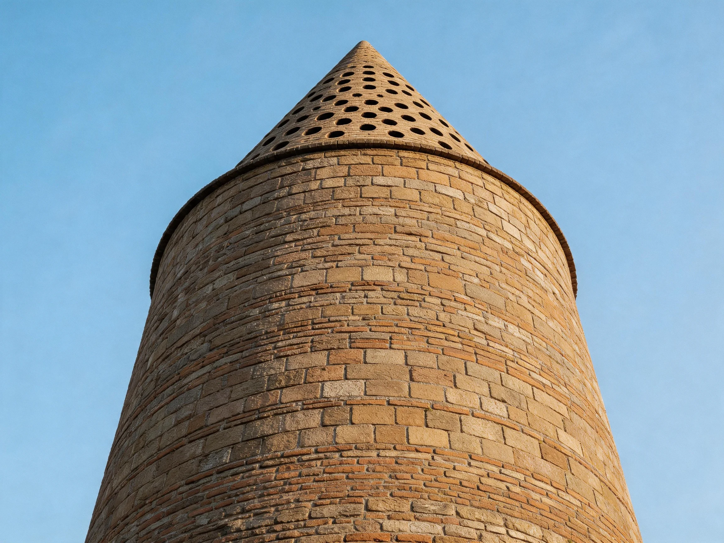 A Tall Brick Tower with a Cone-Capped Structure Against a Clear Blue Sky