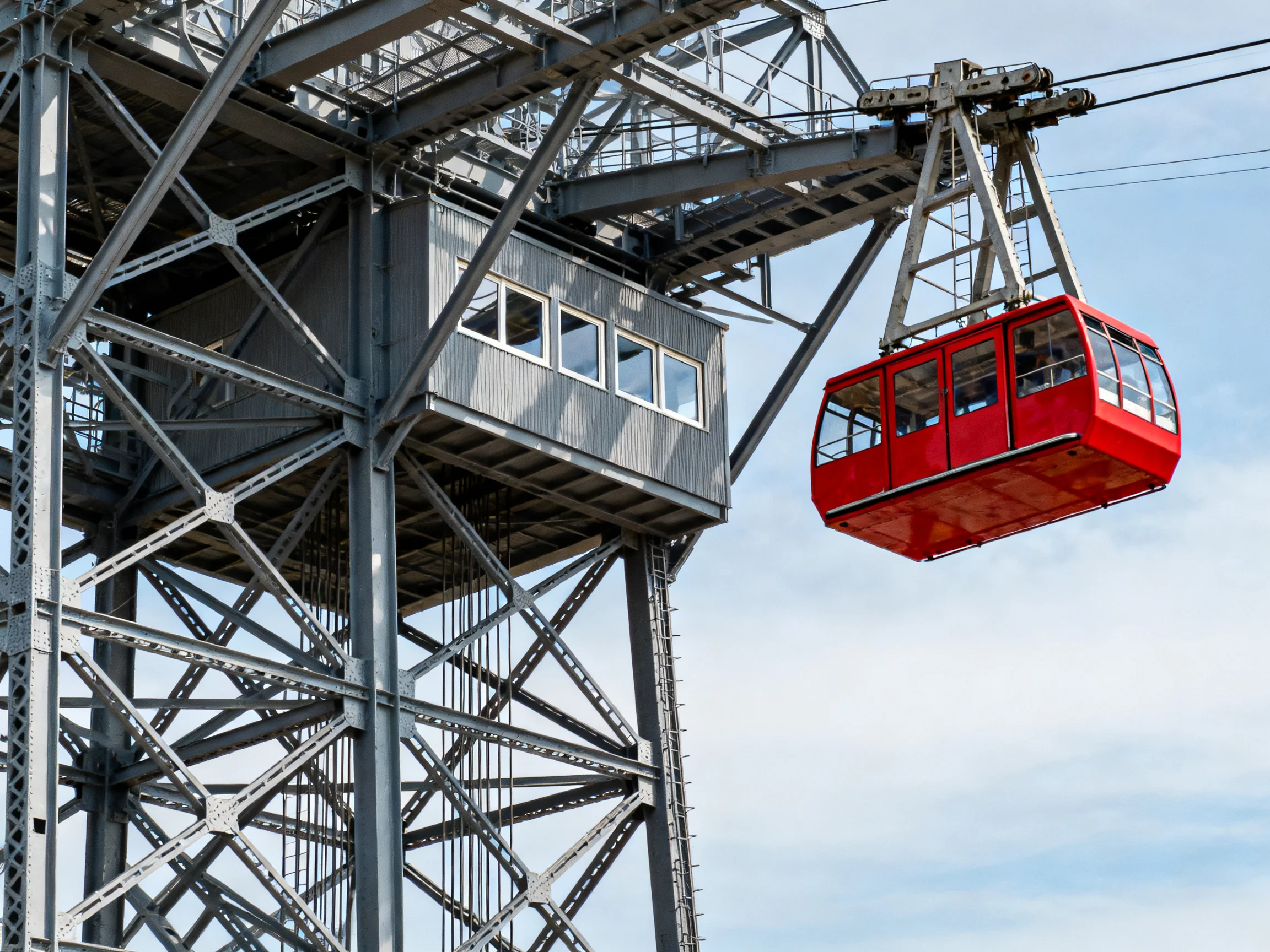A bright red cable car suspended from an industrial steel tower
