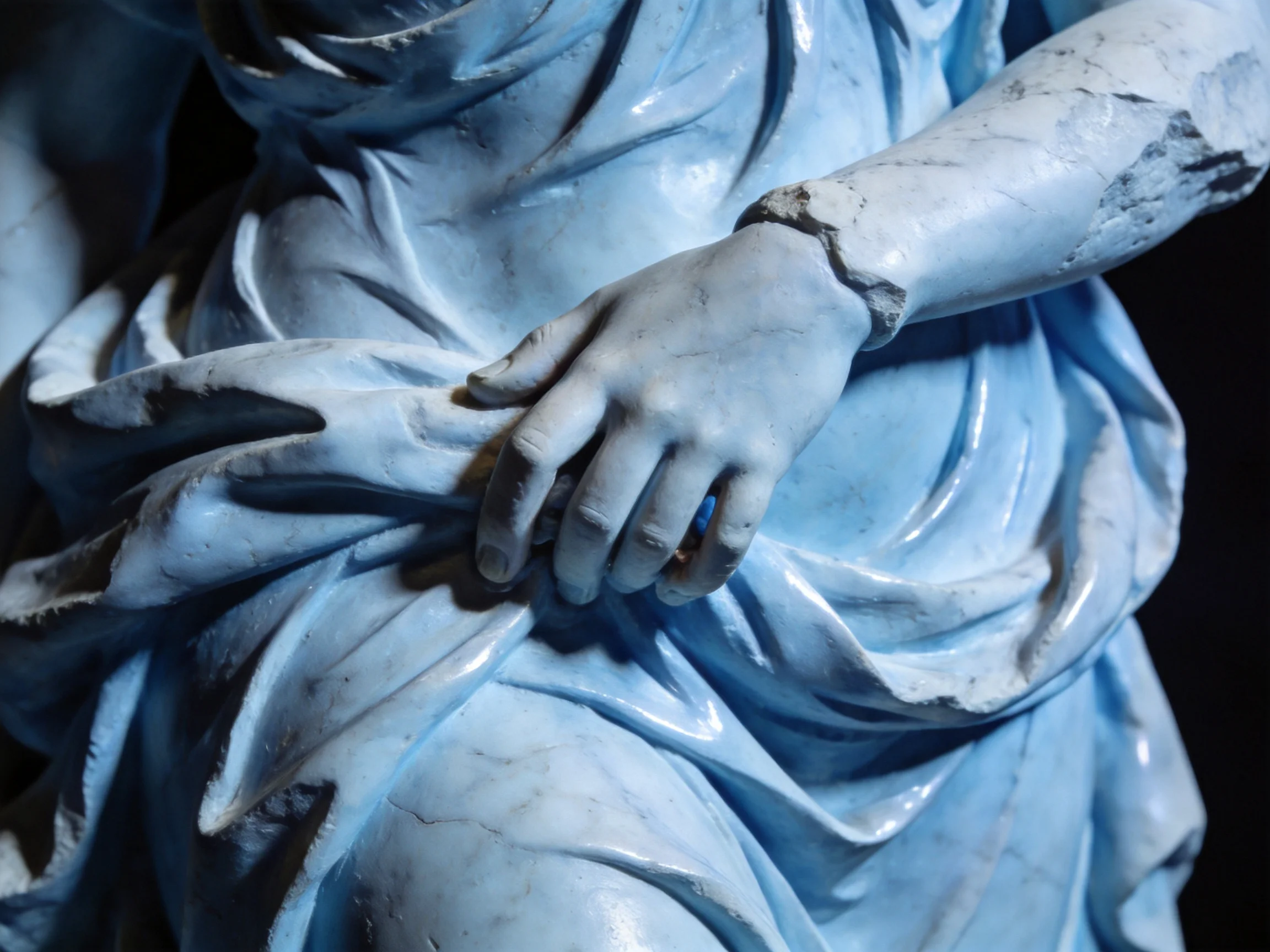 A close - up of a weathered blue statue with draped fabric