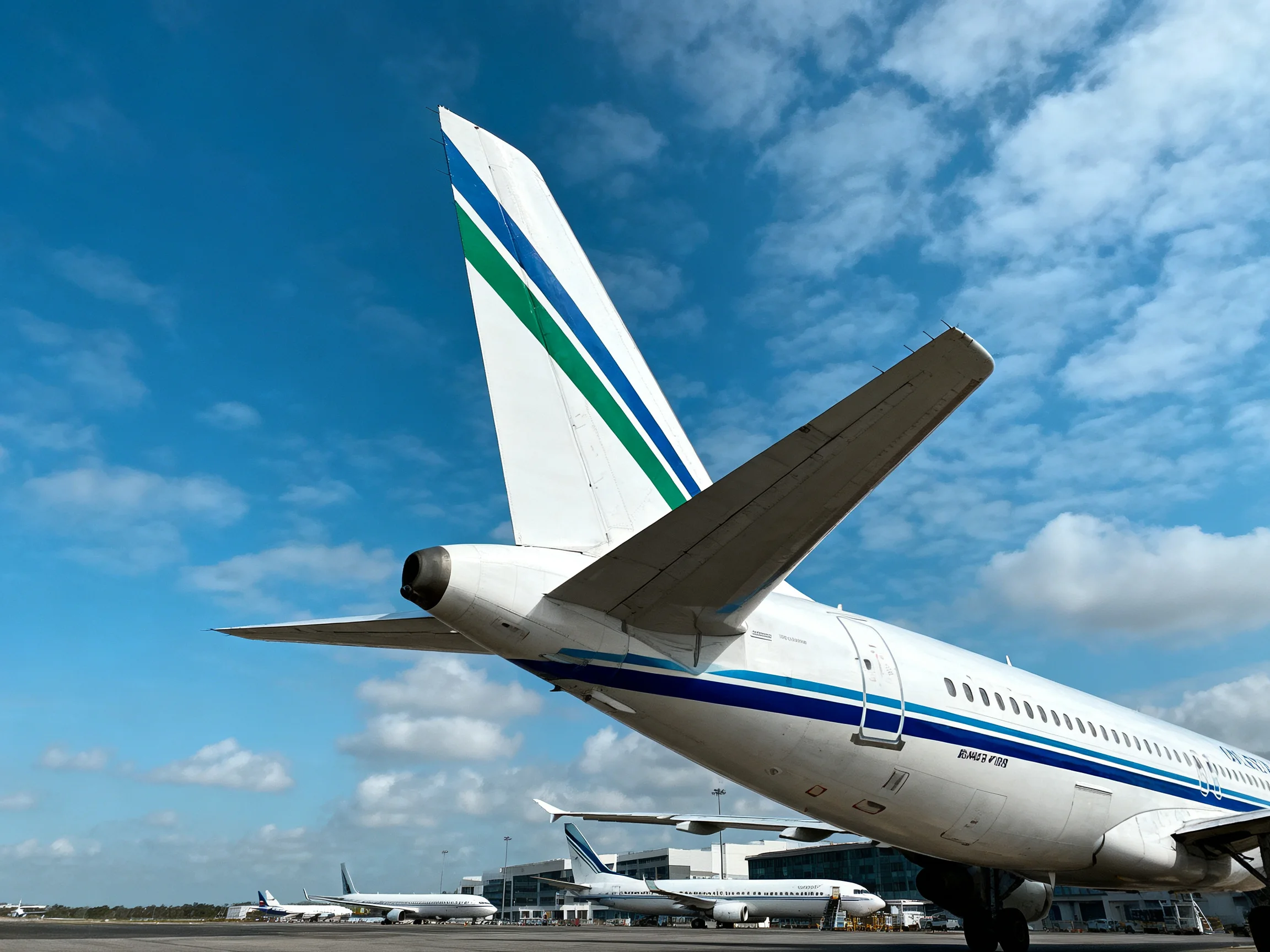A commercial jet’s tail with blue and green stripes on a sunny day