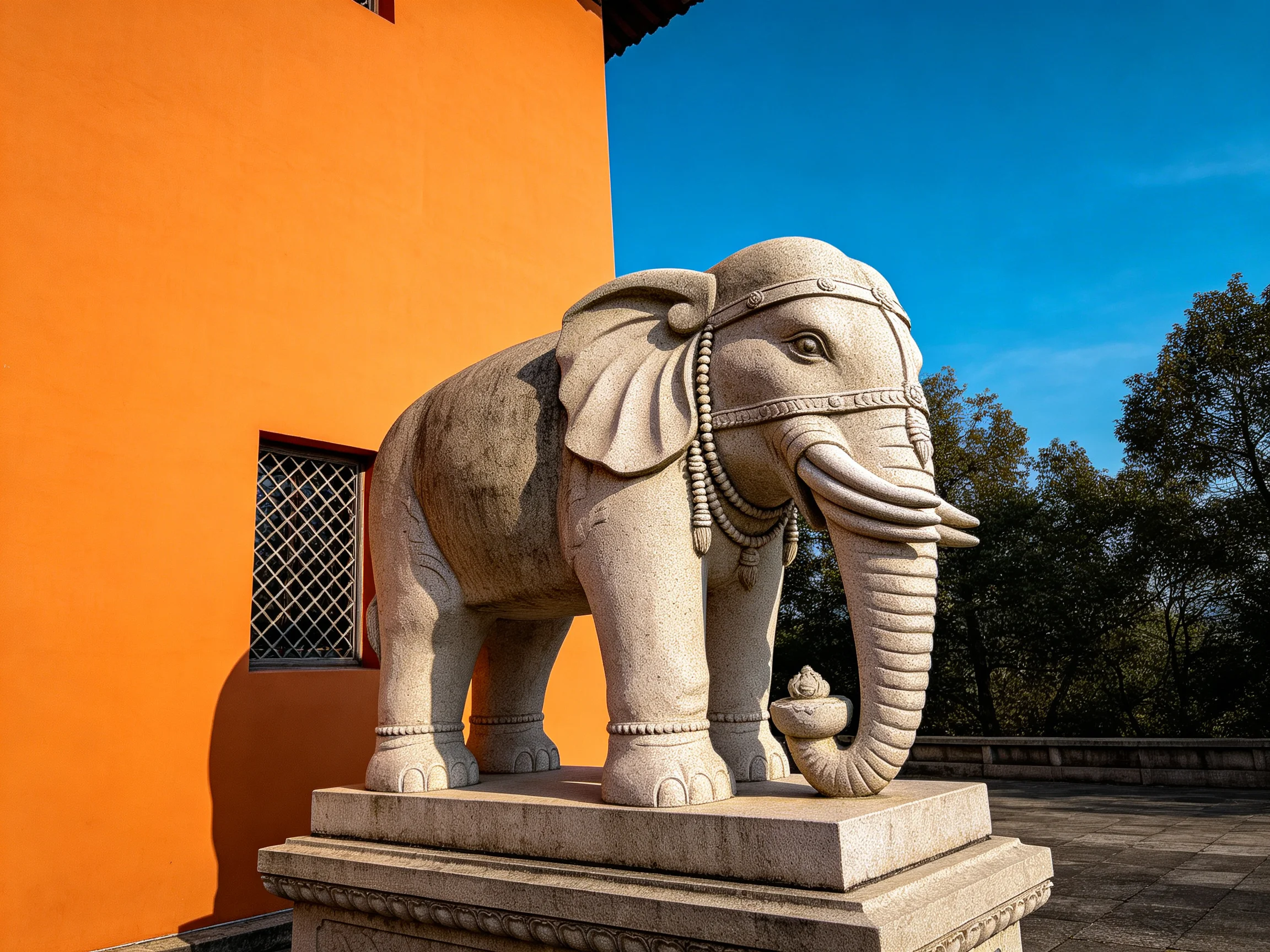 A detailed stone elephant statue beside an orange building under bright blue sky