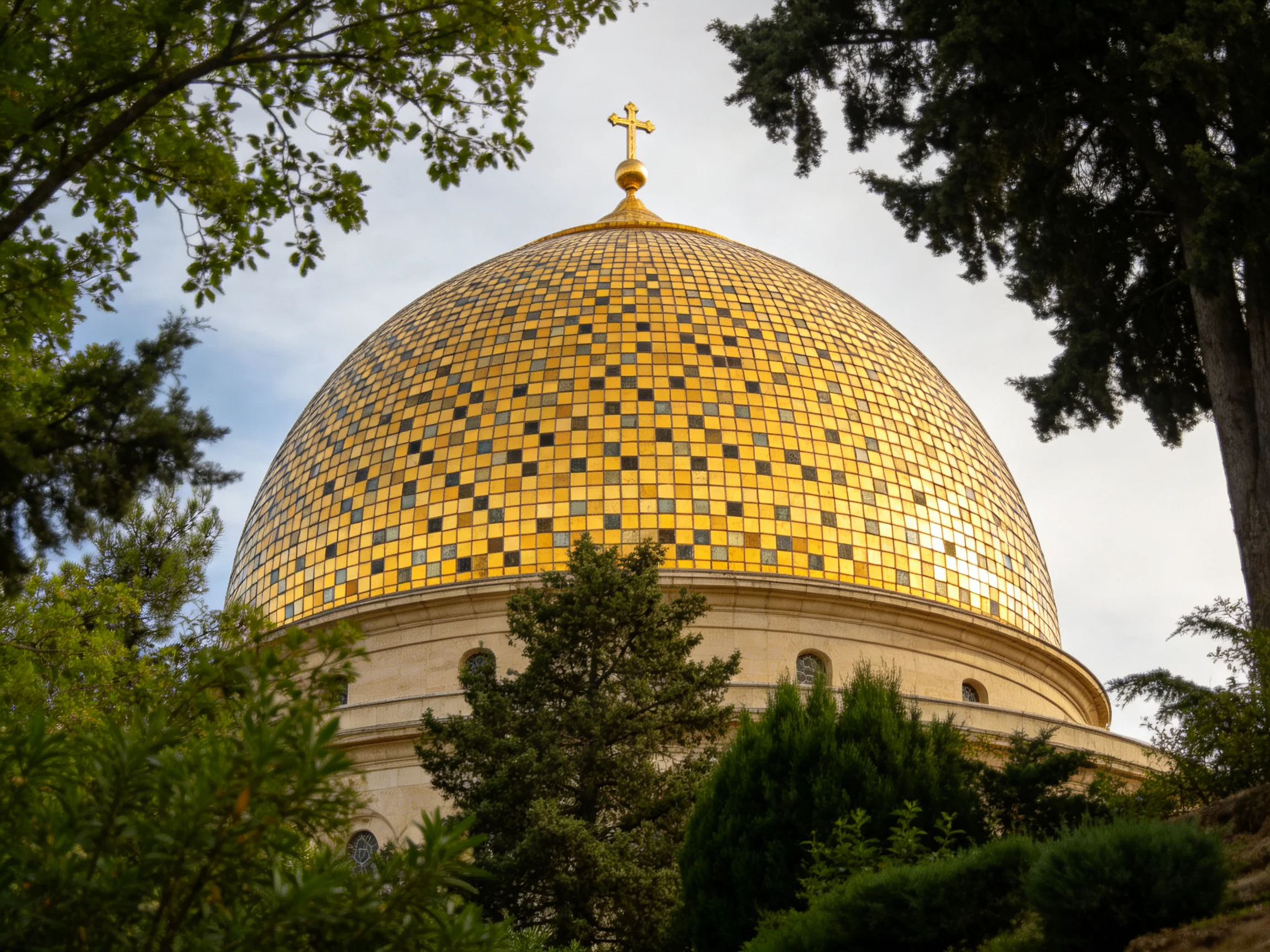 A golden mosaic-domed building with a cross, surrounded by trees
