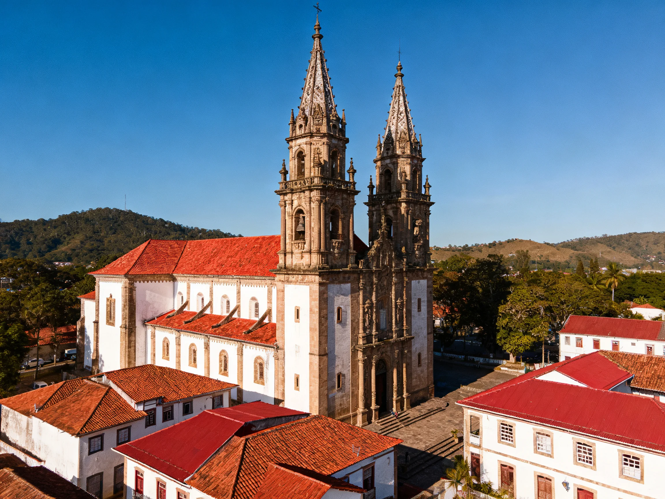 A grand church with twin spires, red roofs, and white walls amid town buildings