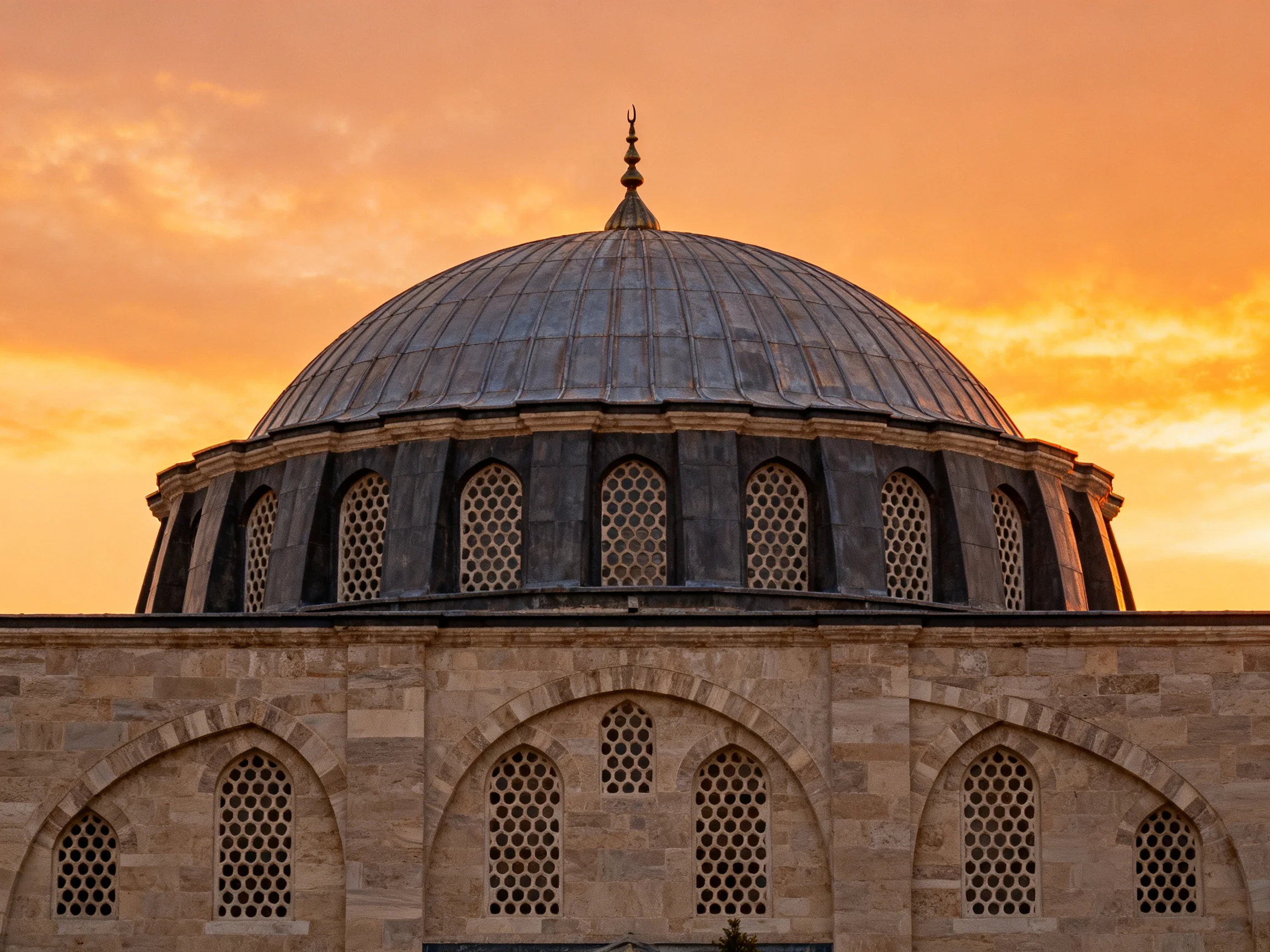 A grand domed architectural structure with an orange-hued sunset backdrop