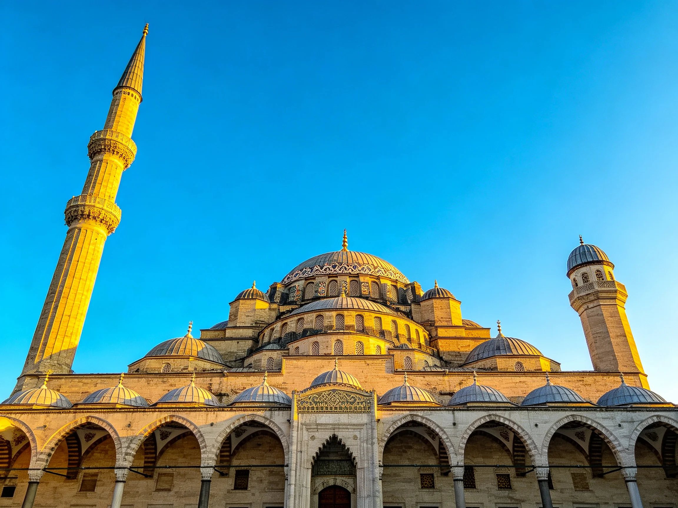 A grand mosque with golden domes and minarets under clear blue sky