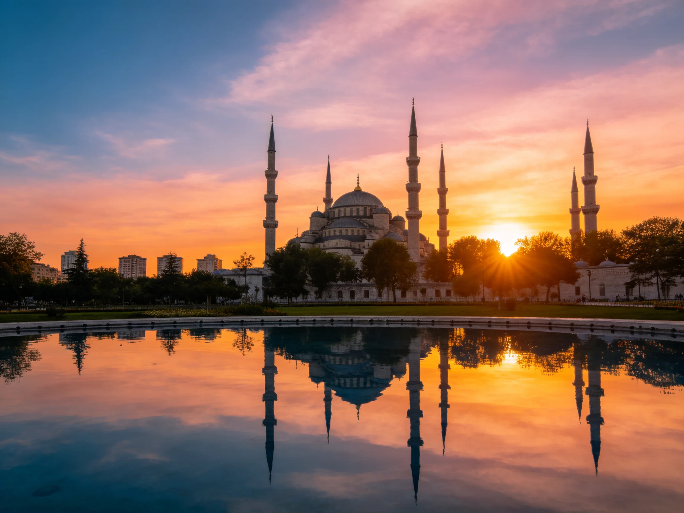 A grand mosque with six minarets reflects in a calm pool at sunset