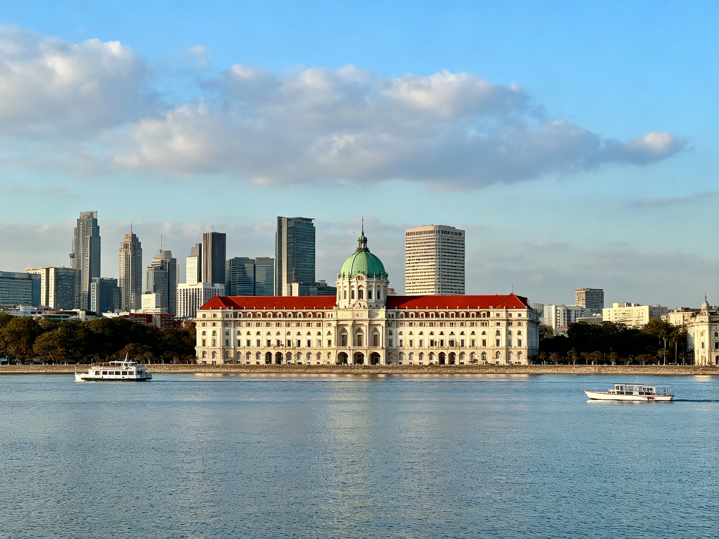 A grand white building with red roof near modern skyscrapers by calm water