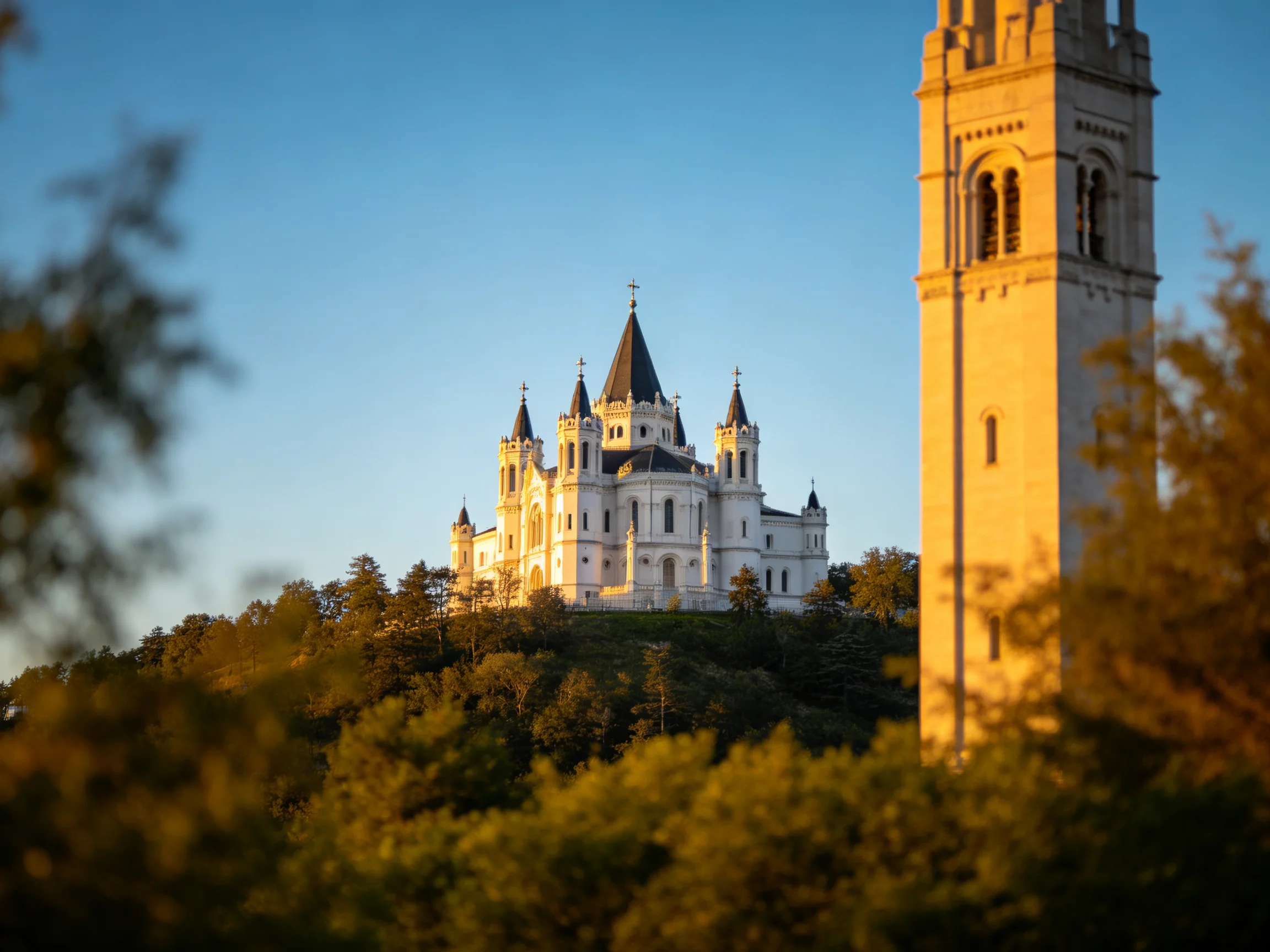A grand white cathedral atop a hill near a tall tower