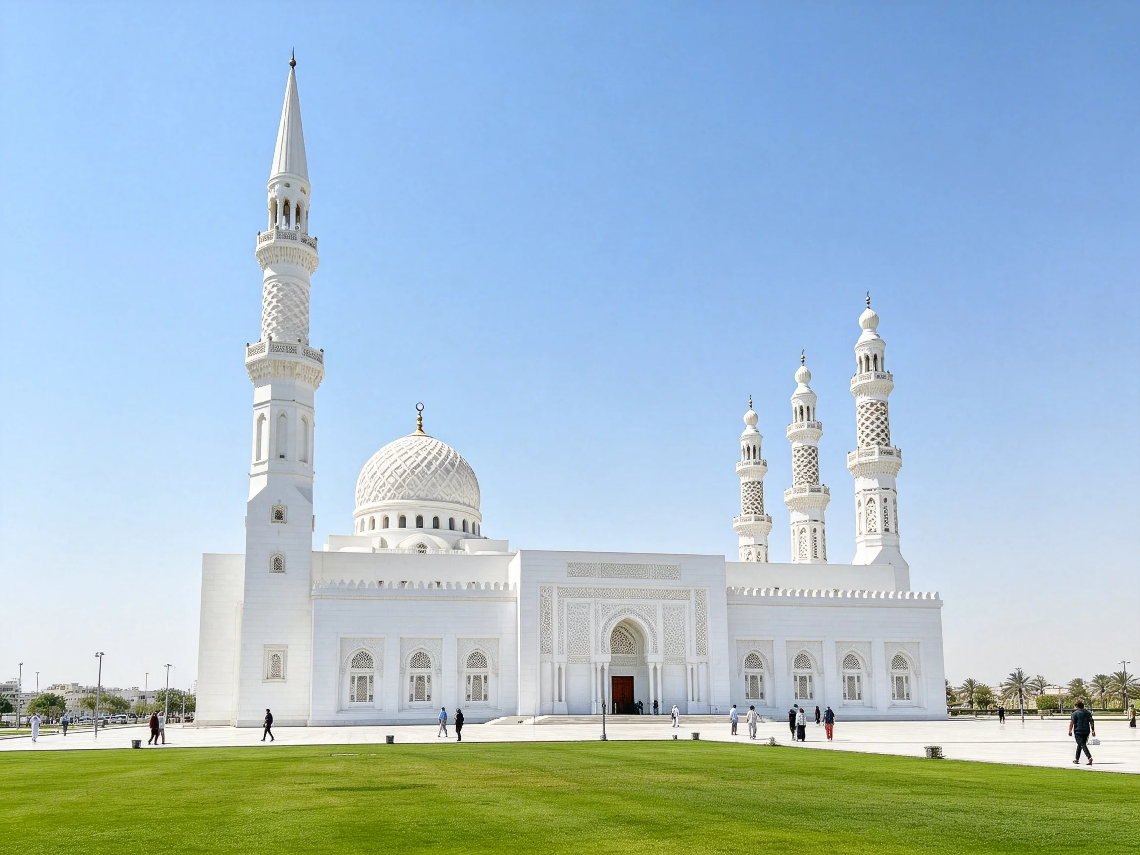 A grand white mosque with four minarets and green lawn under blue sky