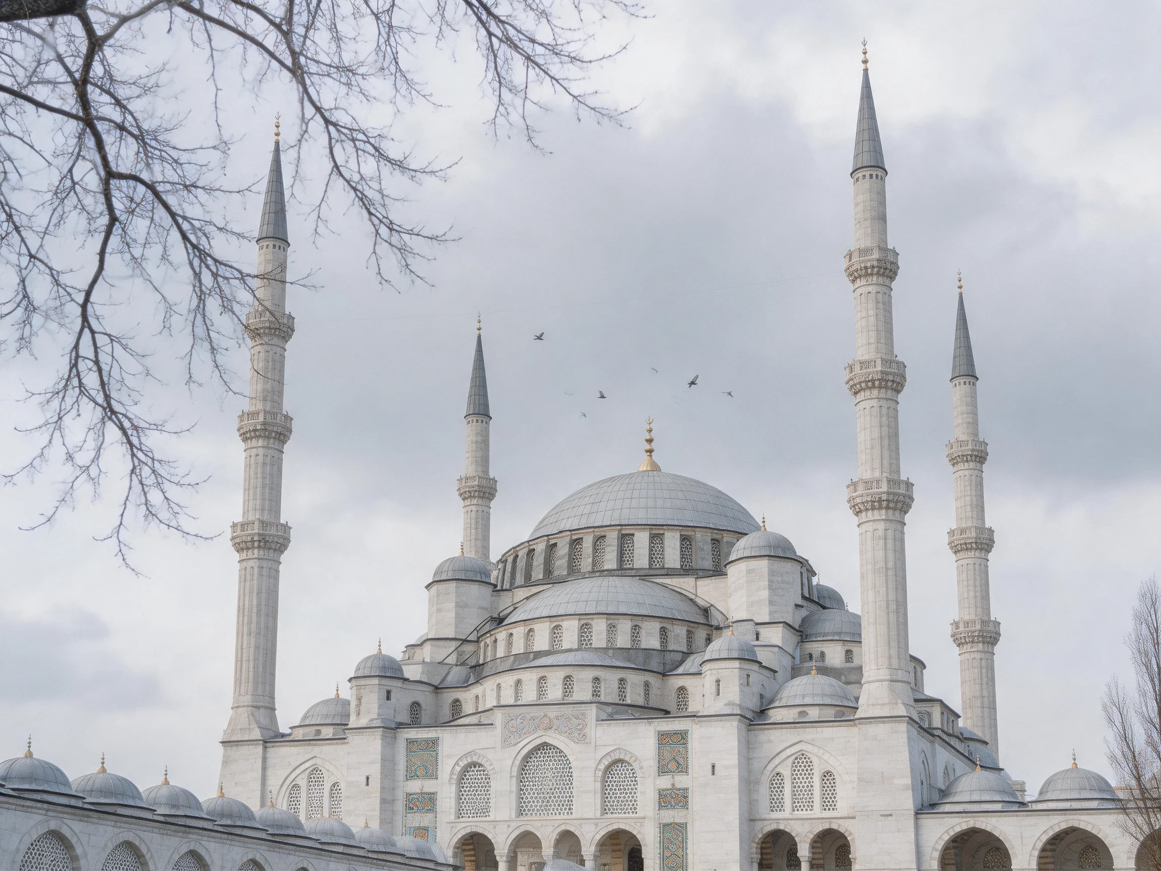 A grand white mosque with four minarets under a cloudy sky