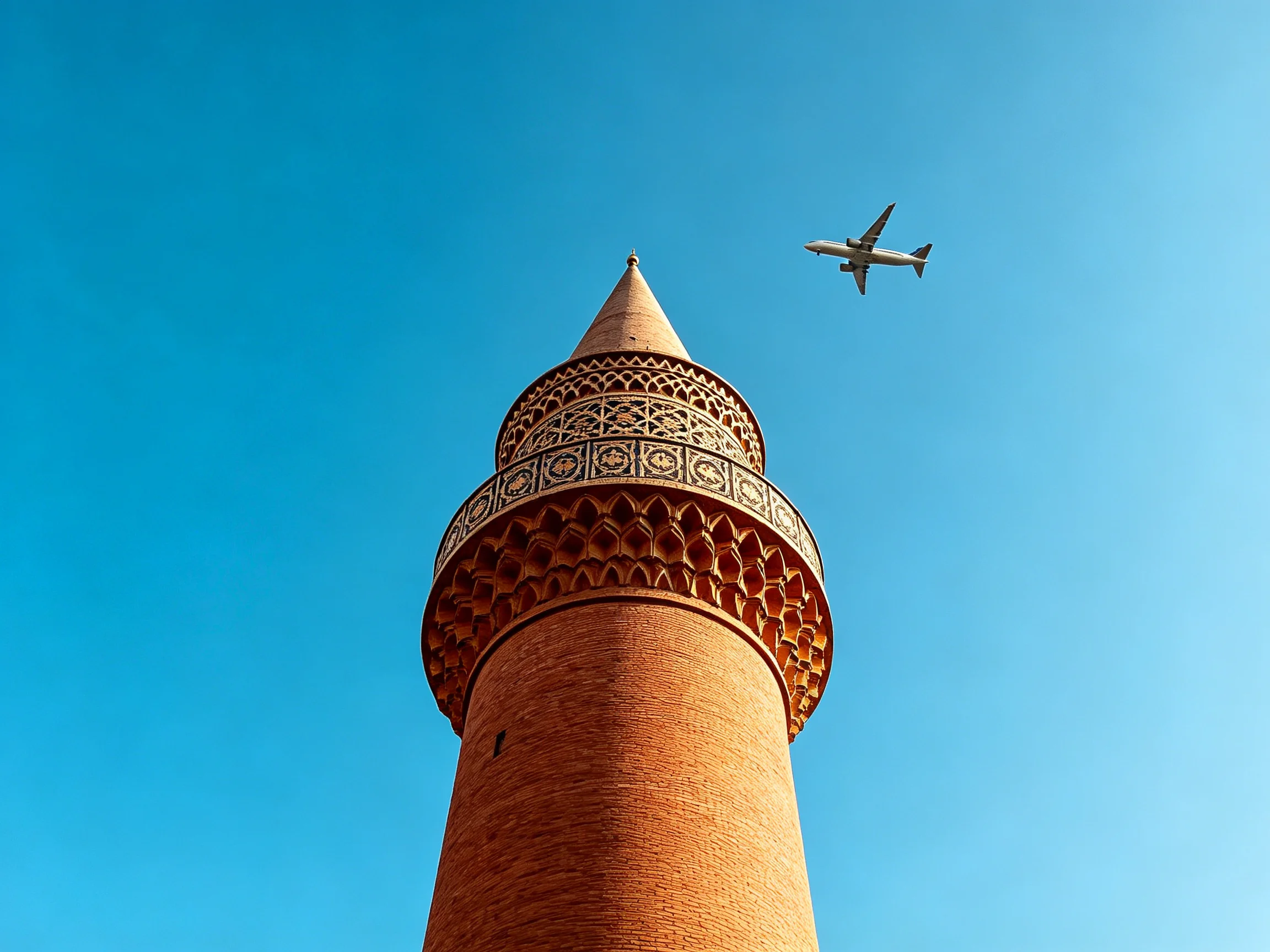 A historic brick minaret towers beside a jet plane under clear blue sky