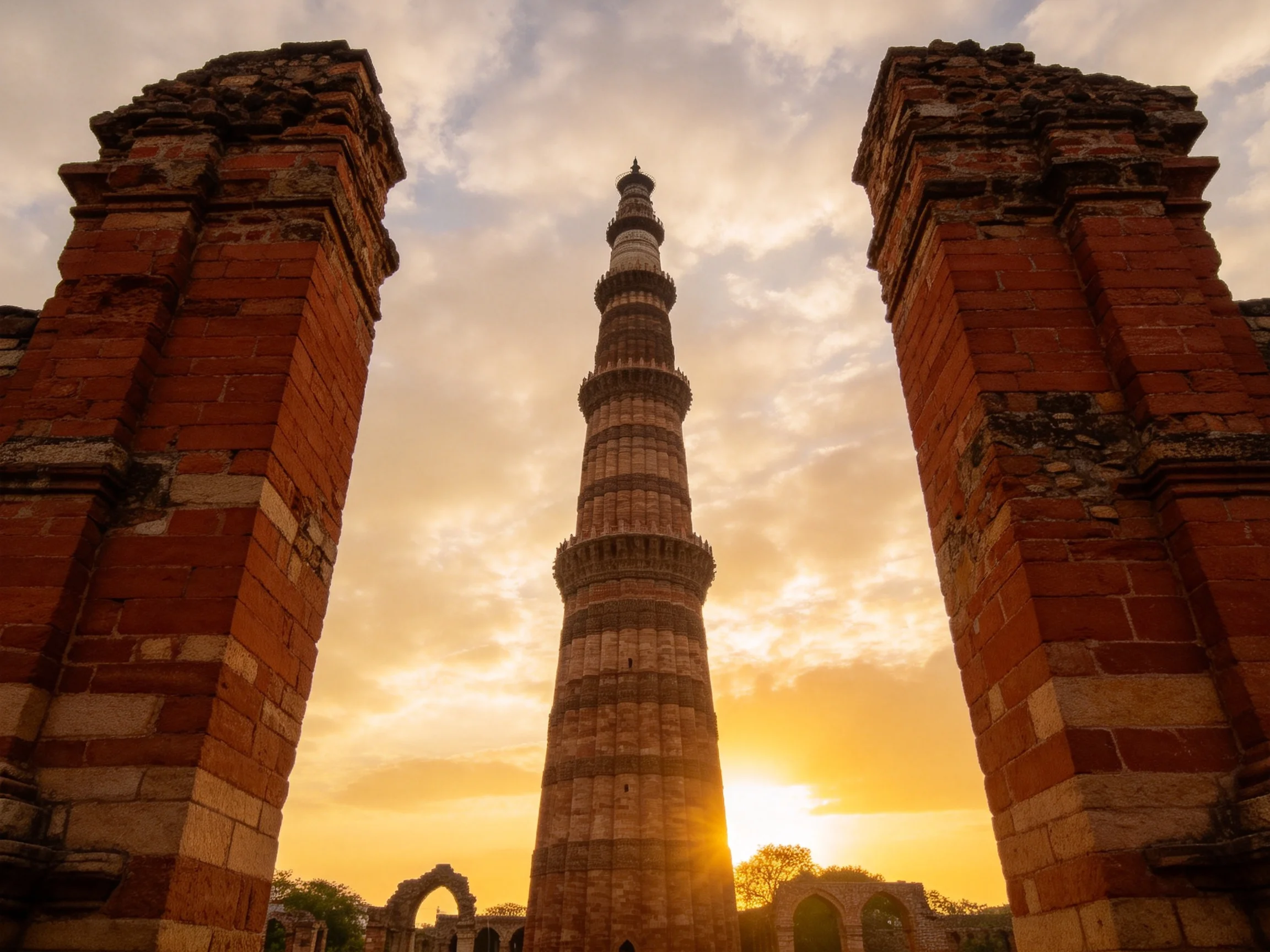 A historic brick tower framed by ancient ruins at sunset