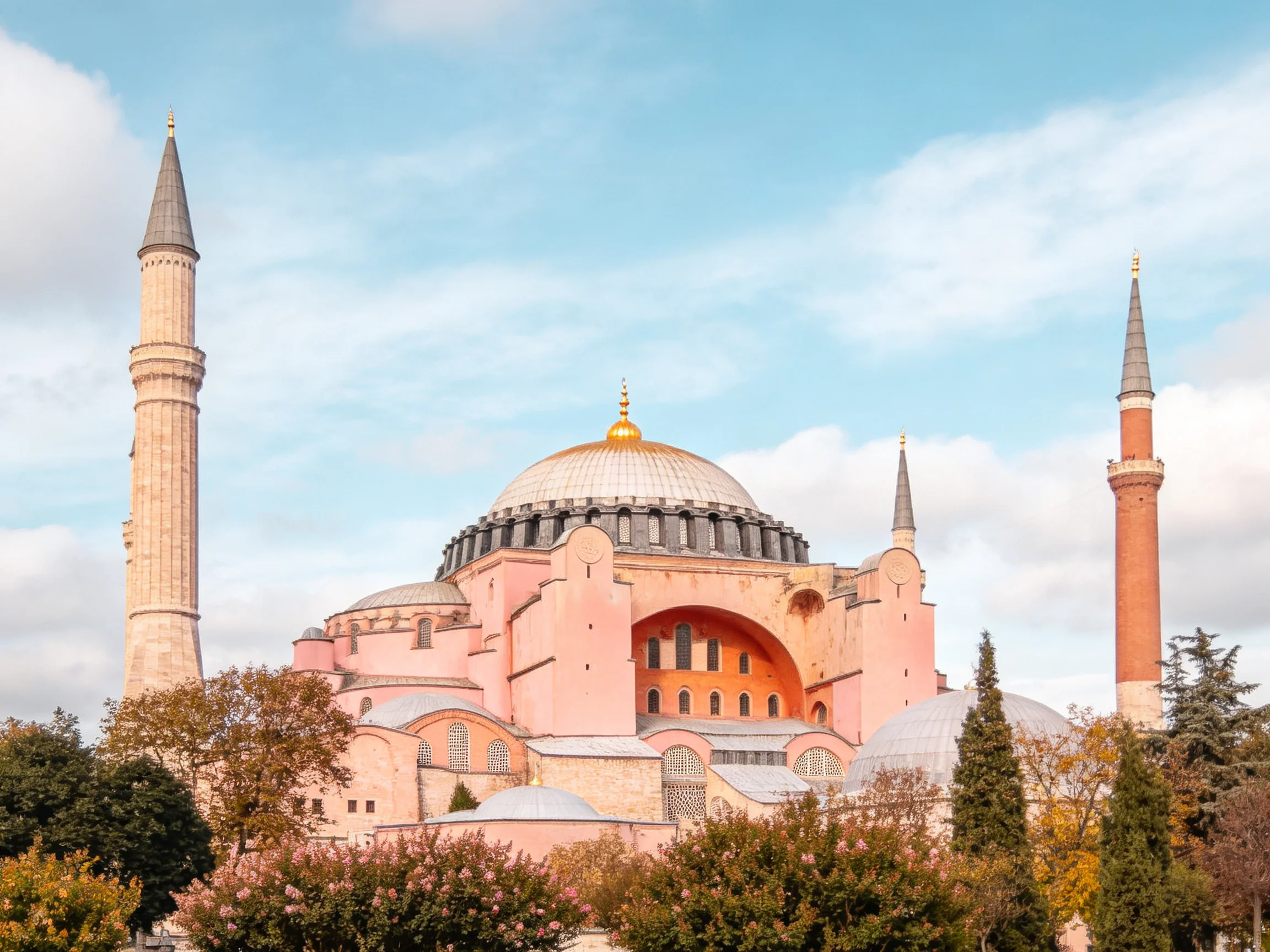 A historic pink-domed structure with tall minarets and autumnal trees