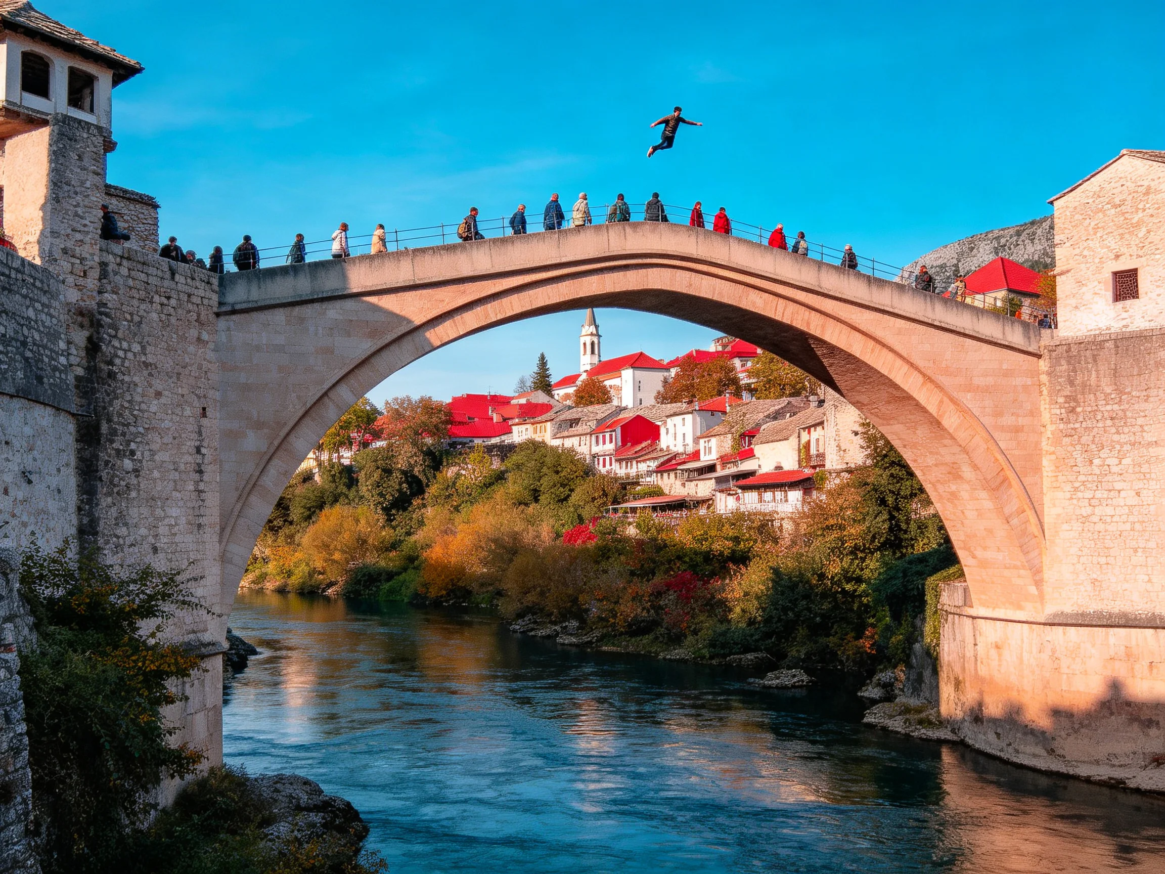 A historic stone bridge spans a blue river near red-roofed buildings