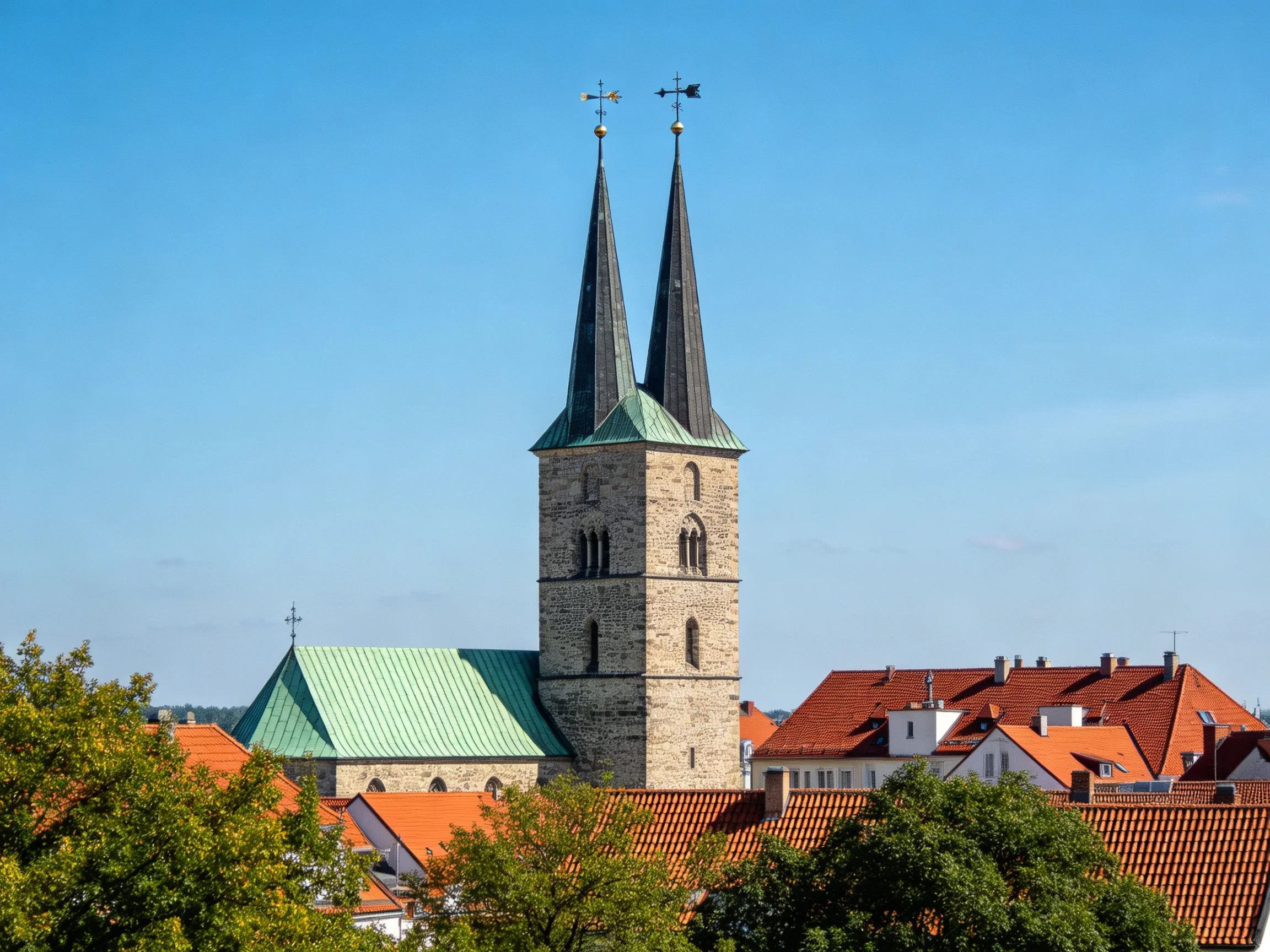 A historic stone church tower with twin spires amid red-roofed buildings