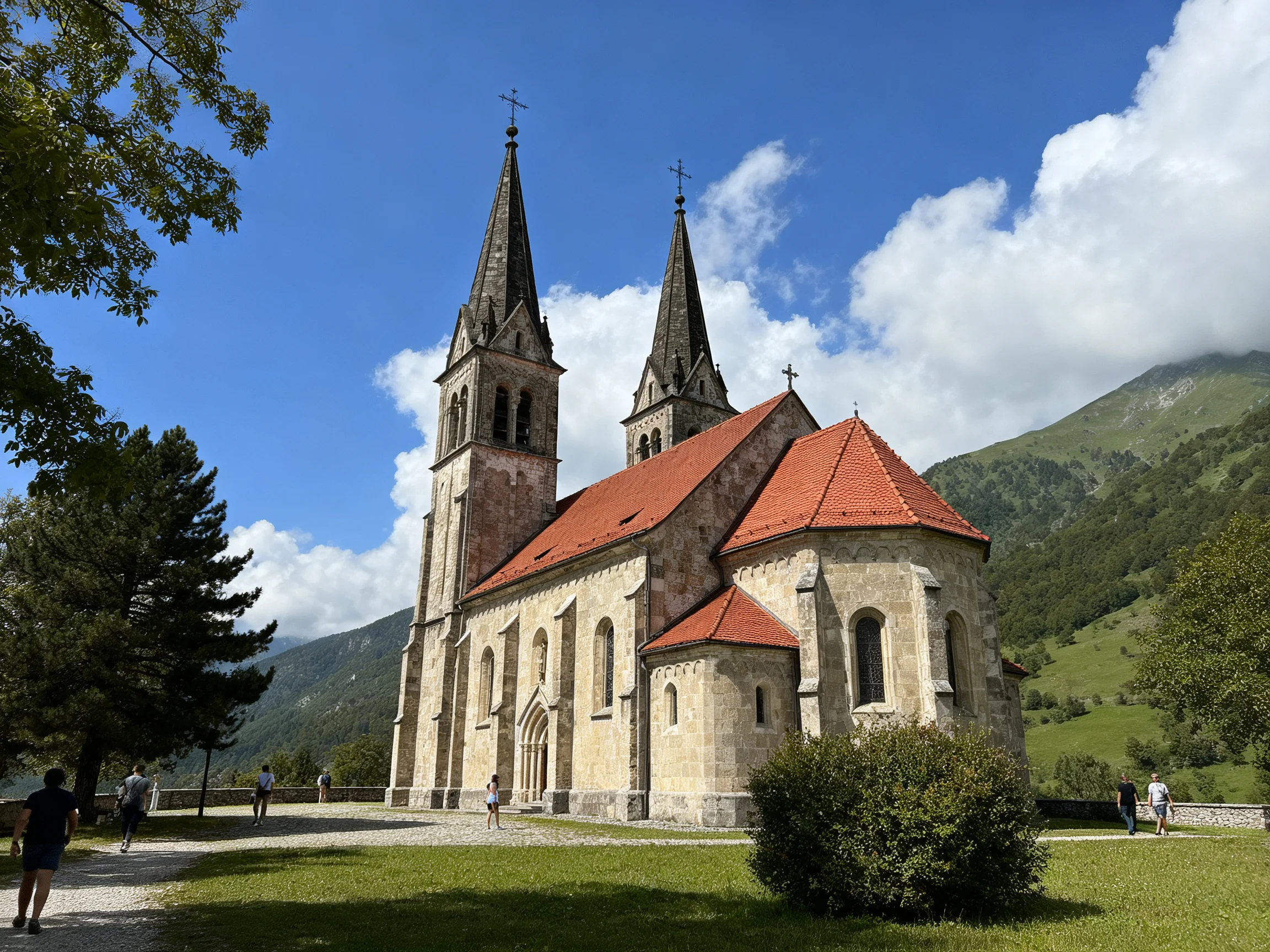 A historic stone church with two spires, red roofs, near green mountains