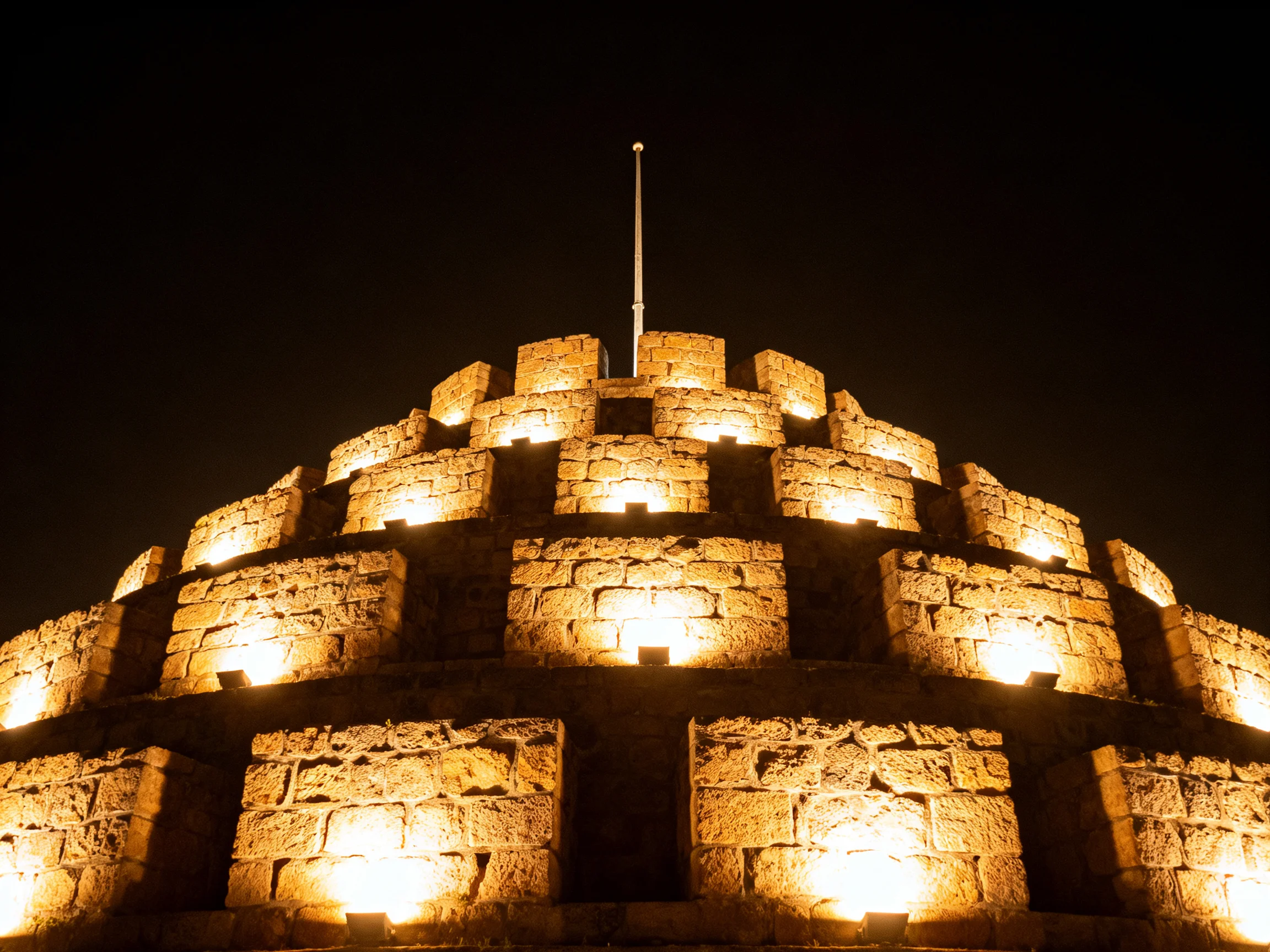 A historic stone pyramid fortress illuminated by golden lights at night