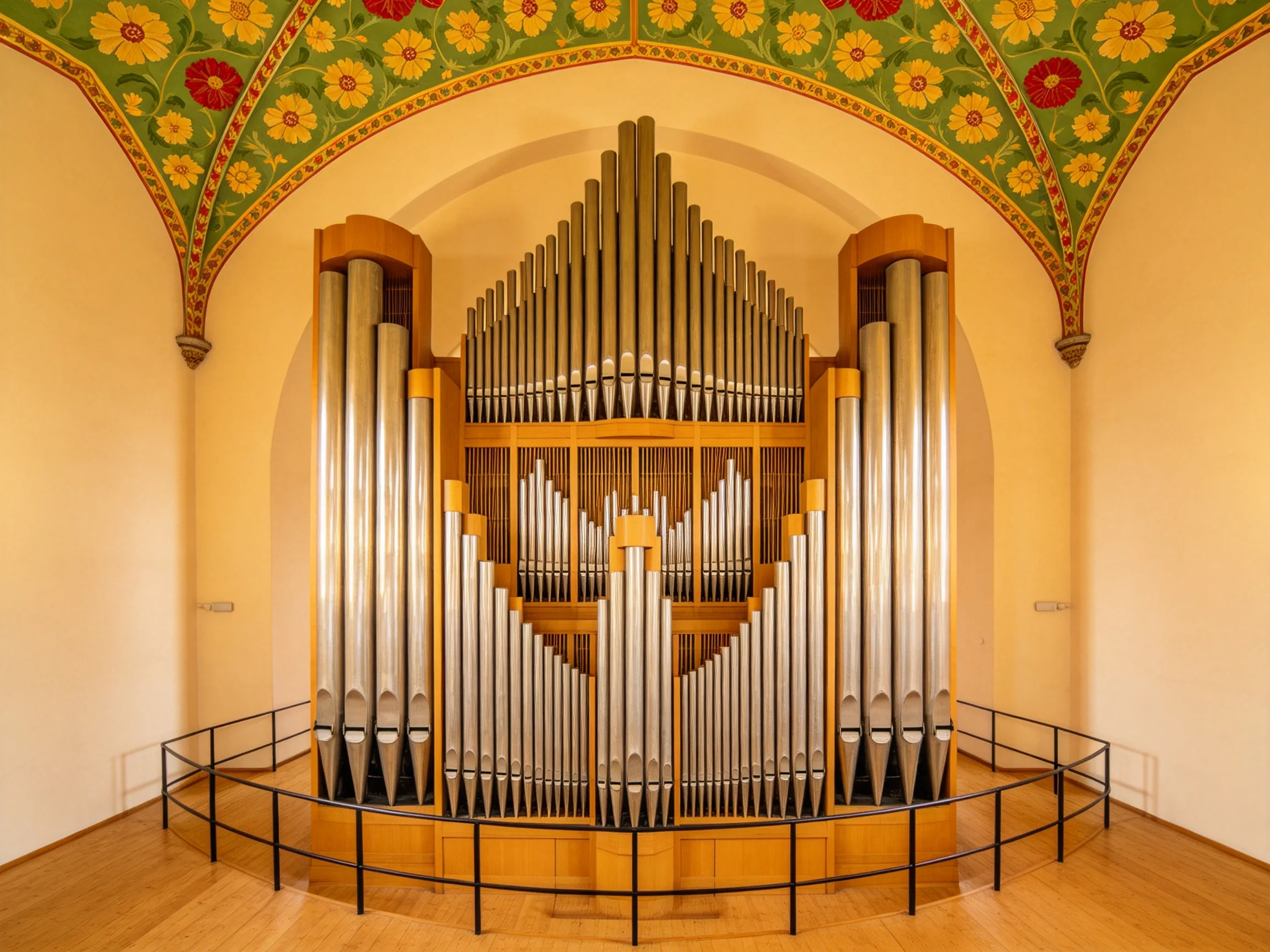 A large pipe organ beneath a vibrantly decorated floral arched ceiling