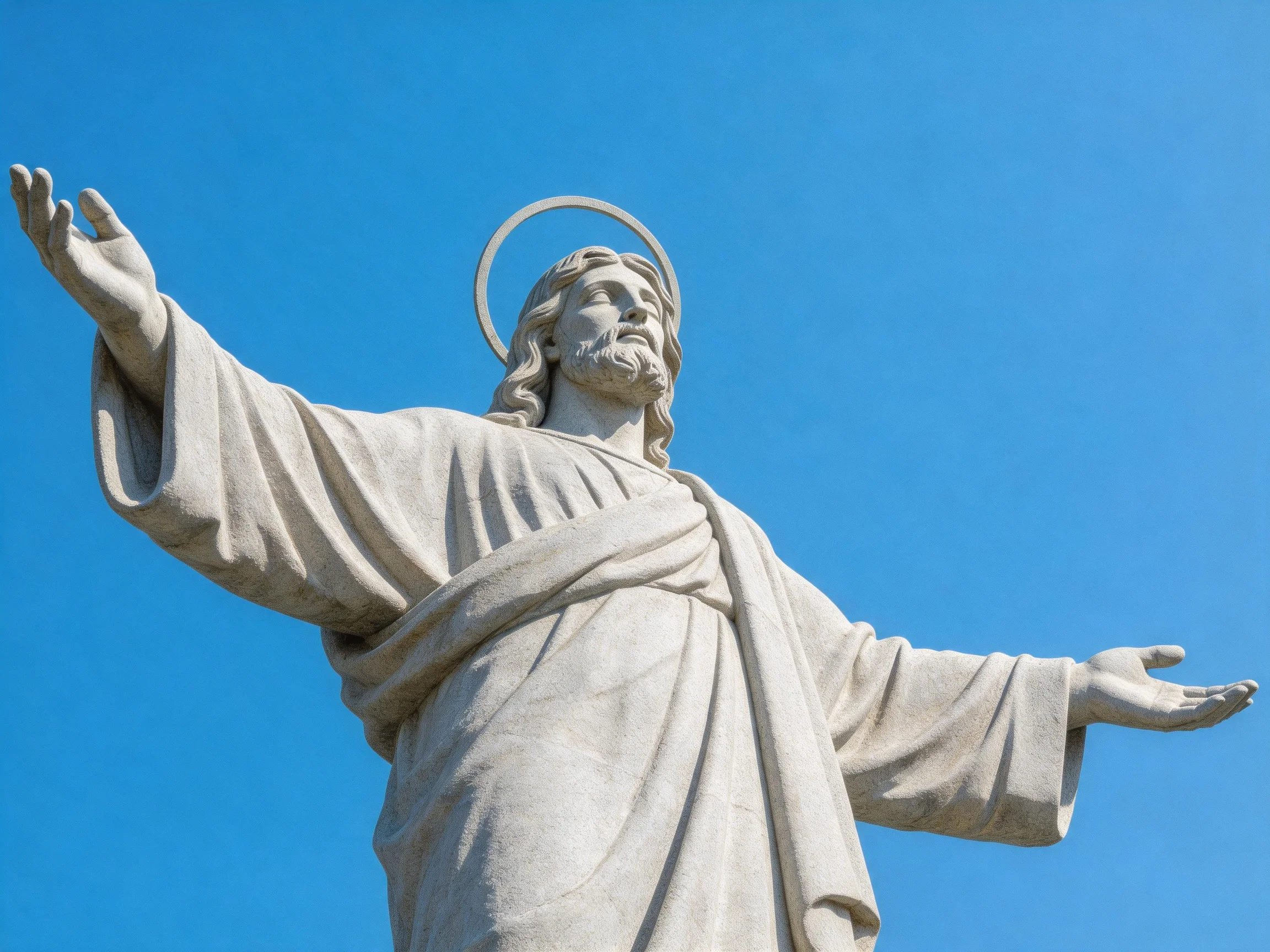 A large white stone statue of Jesus with outstretched arms against clear blue sky