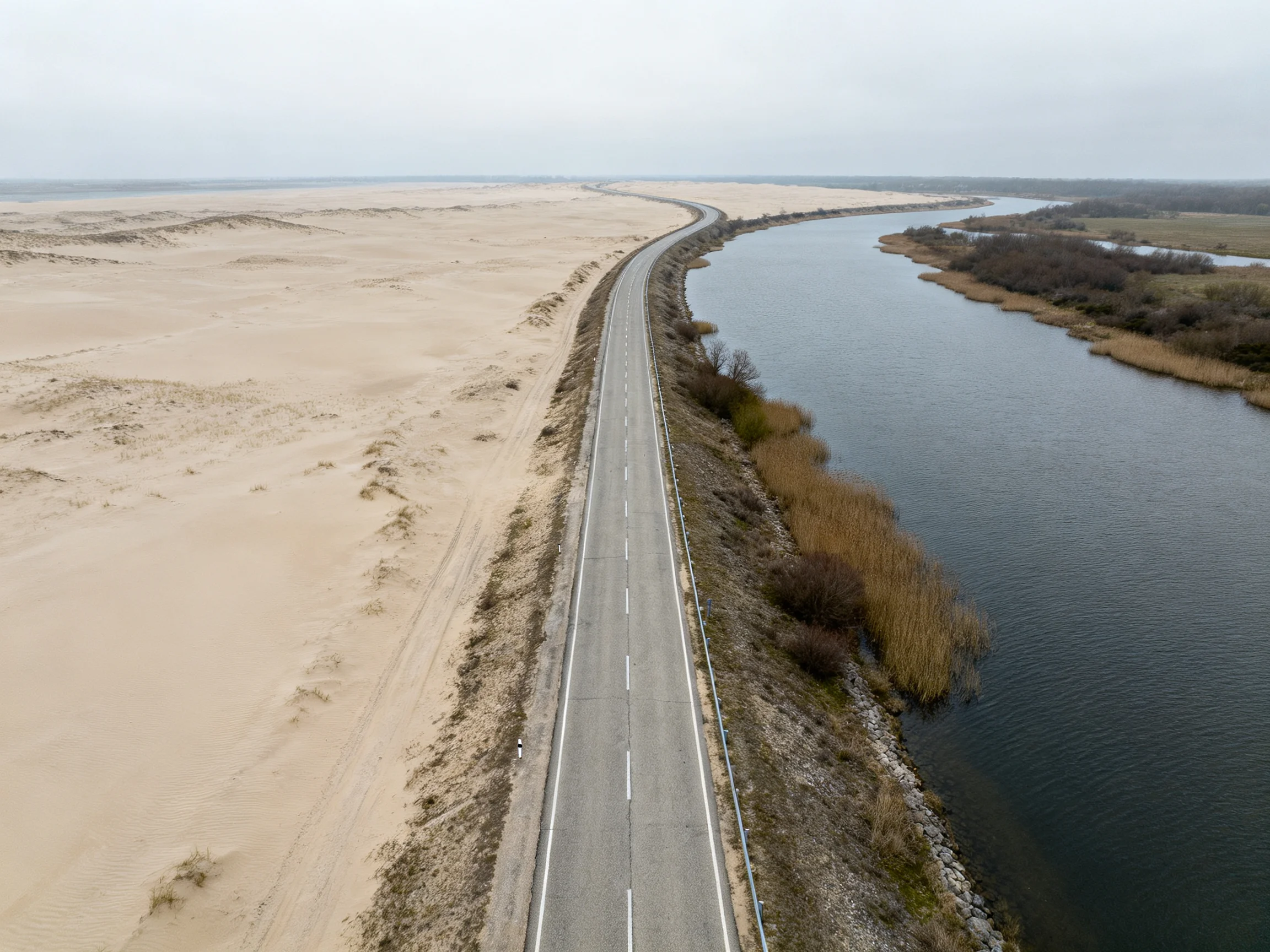 A long road curves beside sandy dunes and a waterway