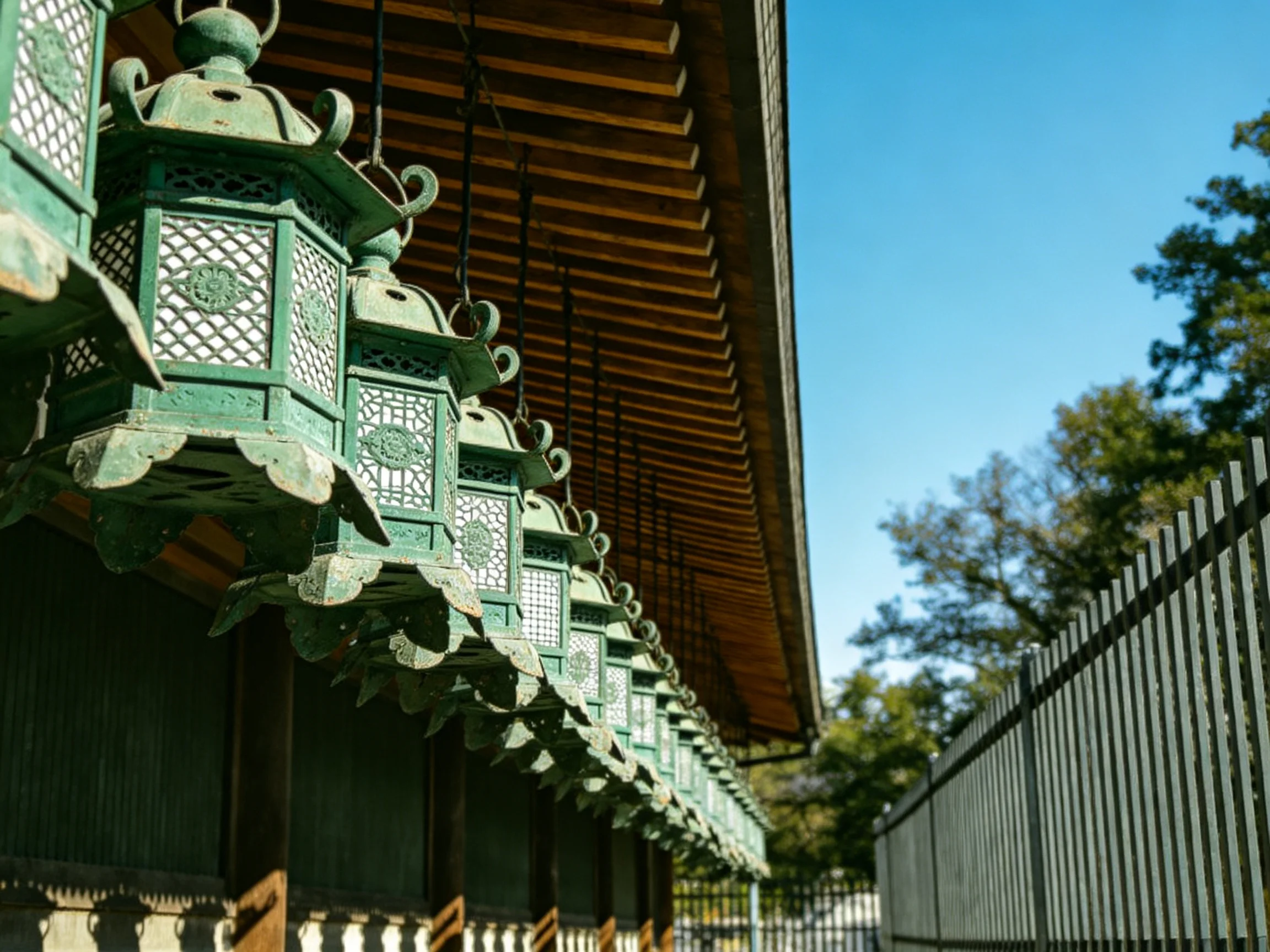 A long row of antique green lanterns hanging from a wooden temple structure