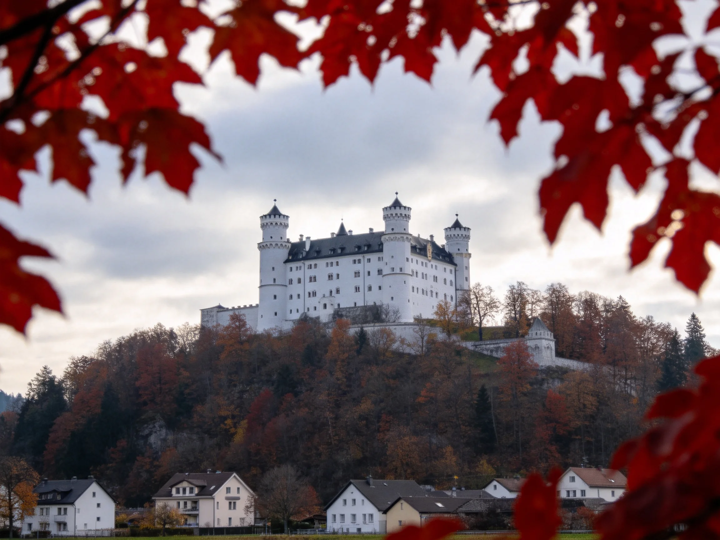 A majestic white castle atop a hill framed by vibrant fall foliage