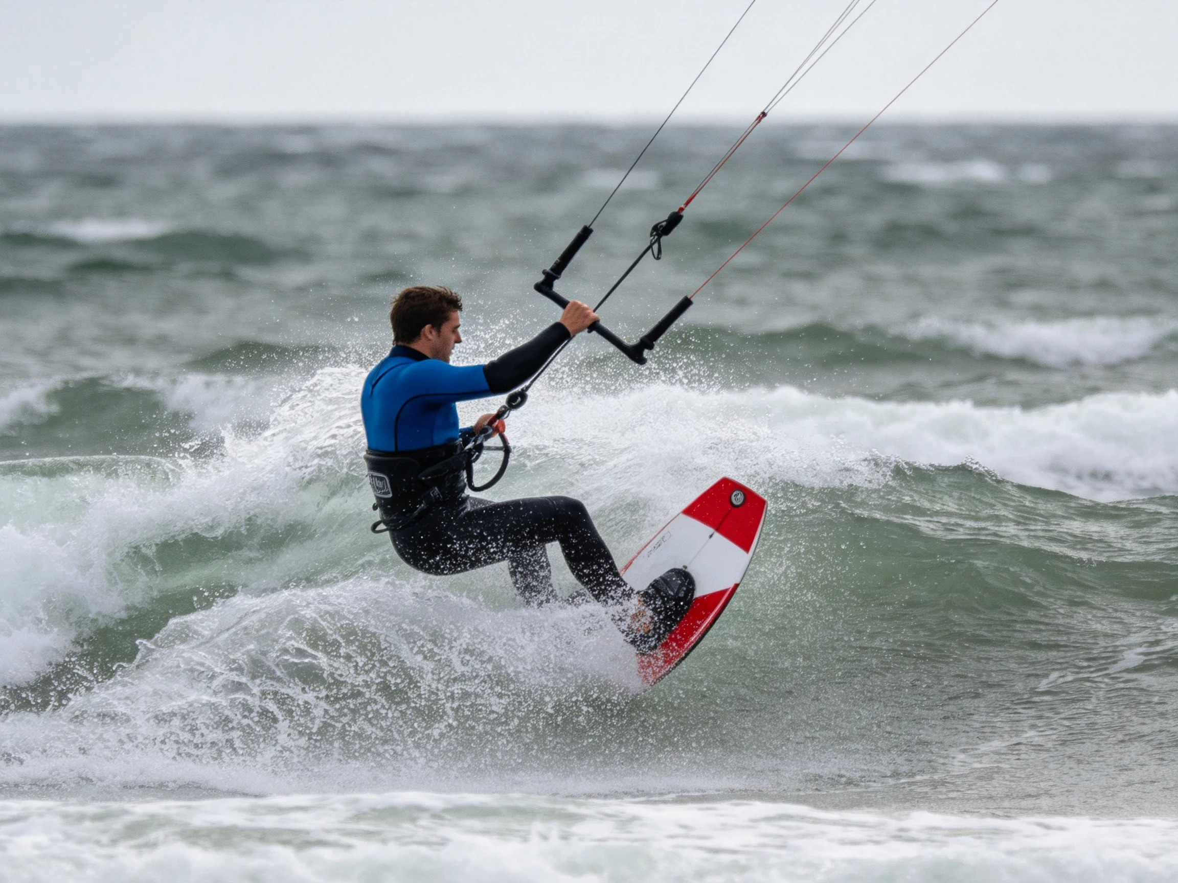 A man kiteboarding on turbulent ocean waters with a red and white board