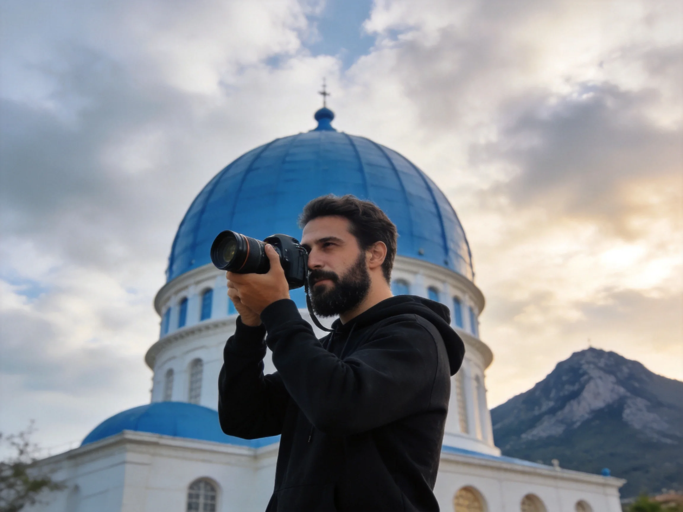 A man photographs a white church with vibrant blue domes near mountains