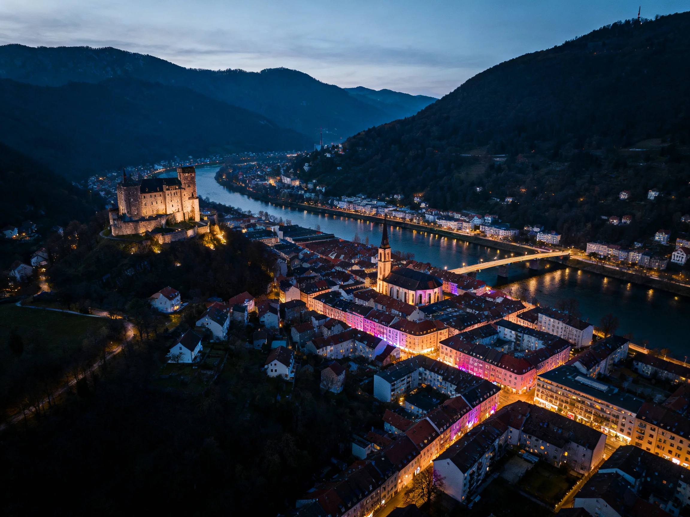 A medieval town with a castle, winding river, and evening illumination