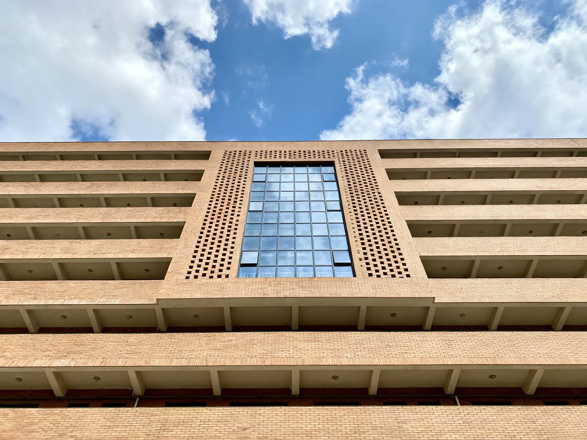 A multi - story brick building with a central glass panel under blue sky