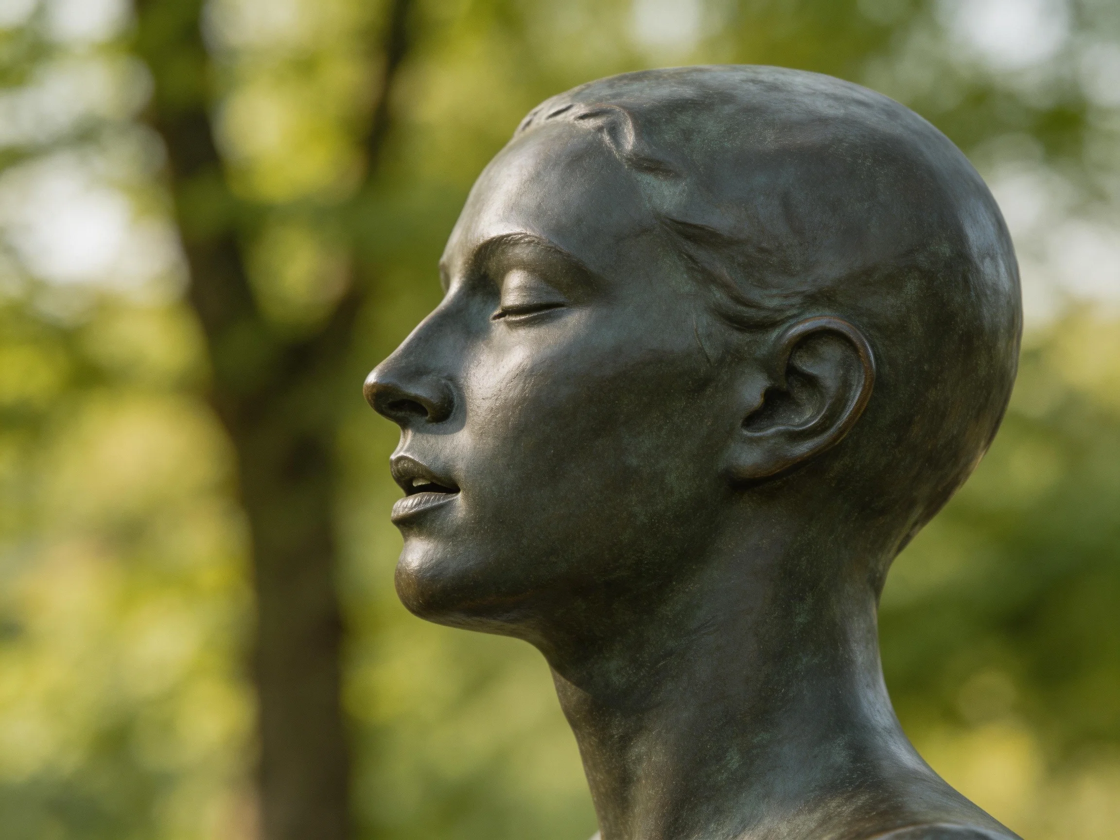 A serene bronze statue of a figure with closed eyes in a green park setting