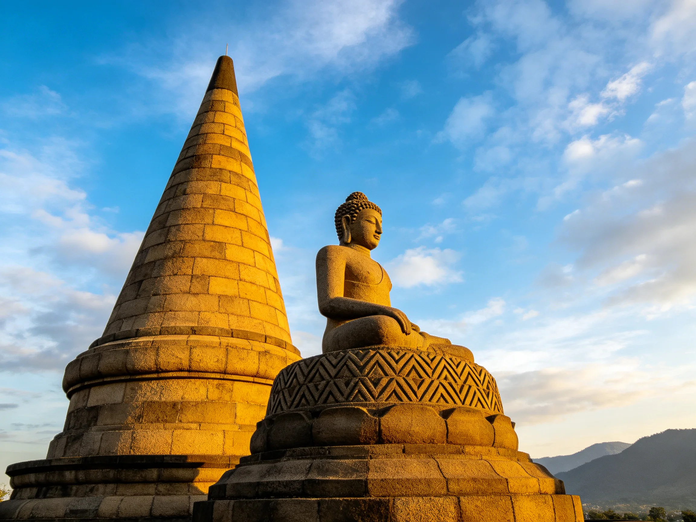A serene stone Buddha statue beside an ancient conical tower under blue skies
