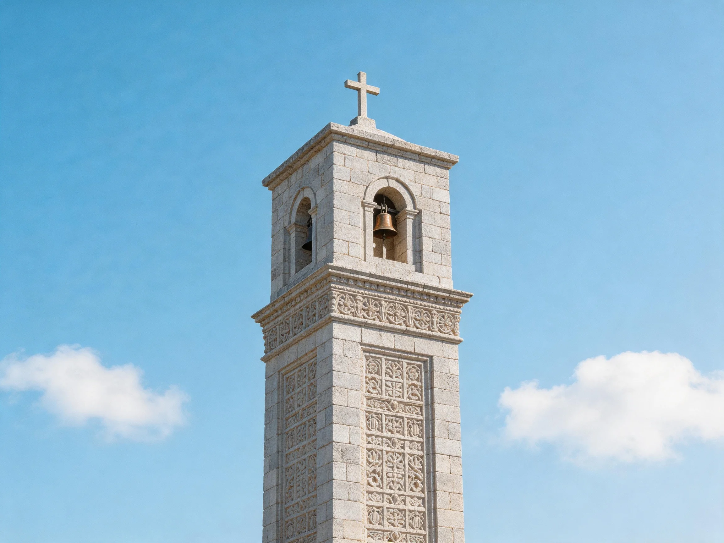 A stone bell tower with a cross under a clear blue sky