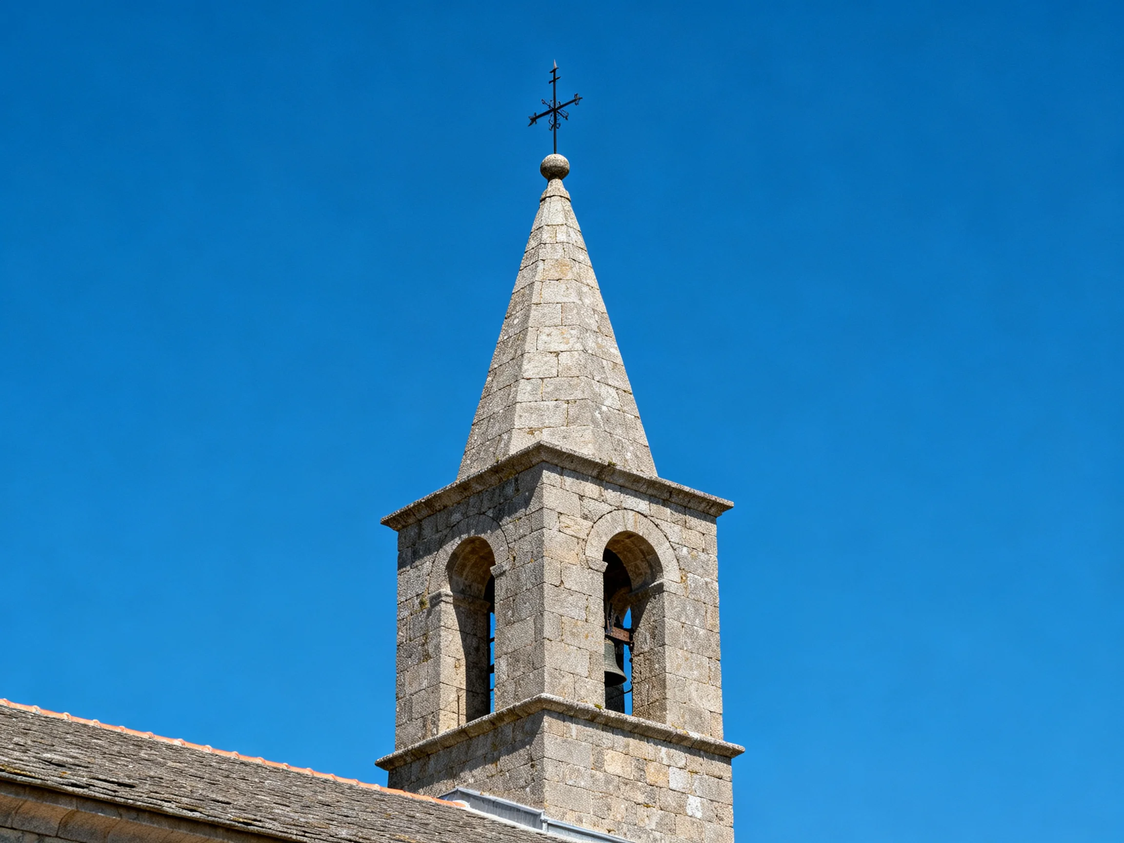 A stone bell tower with a pointed spire and cross
