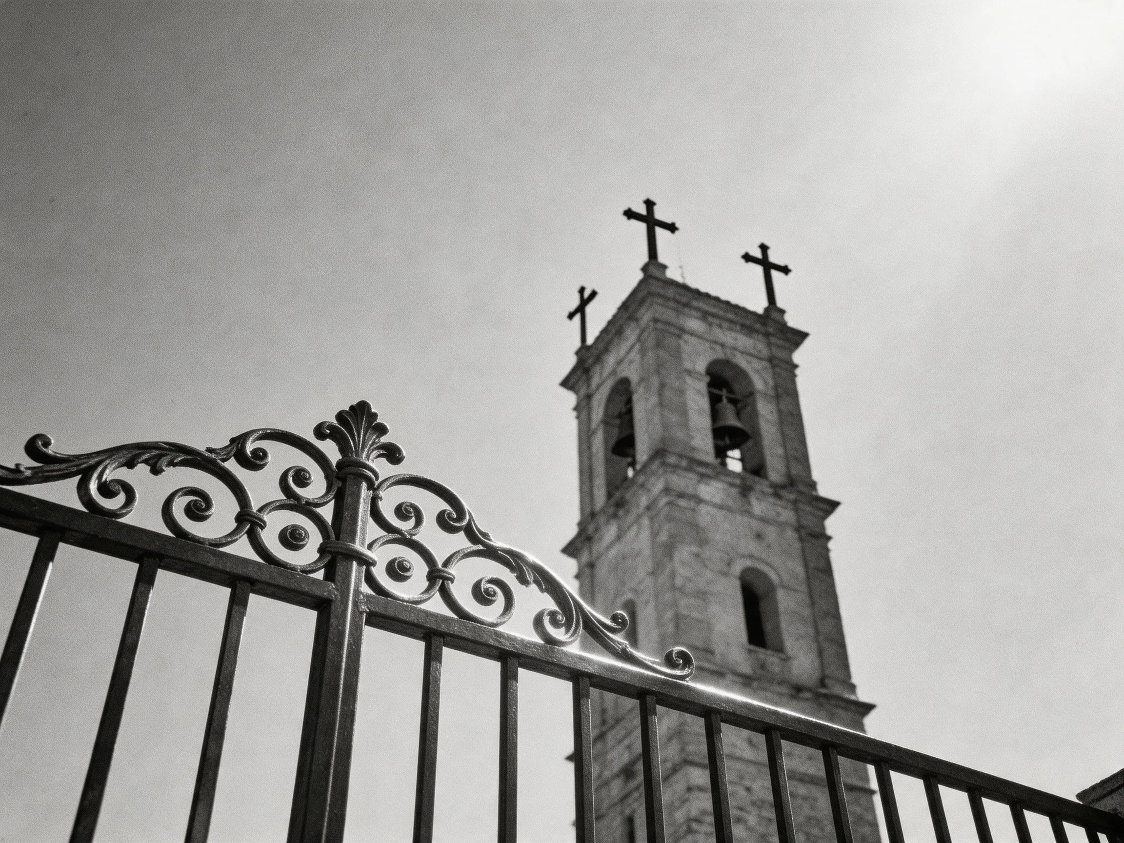 A stone bell tower with three crosses behind an ornate iron fence