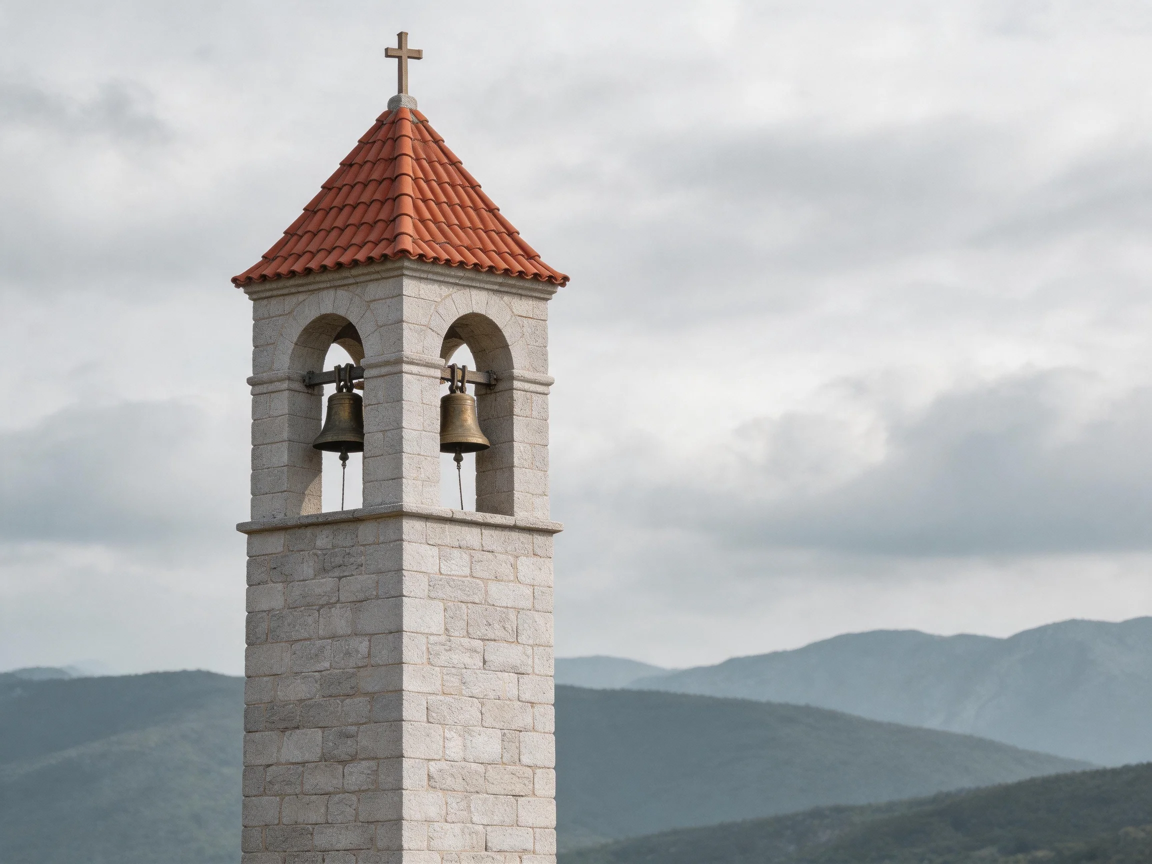 A stone bell tower with two bronze bells and a red-tiled roof near mountains