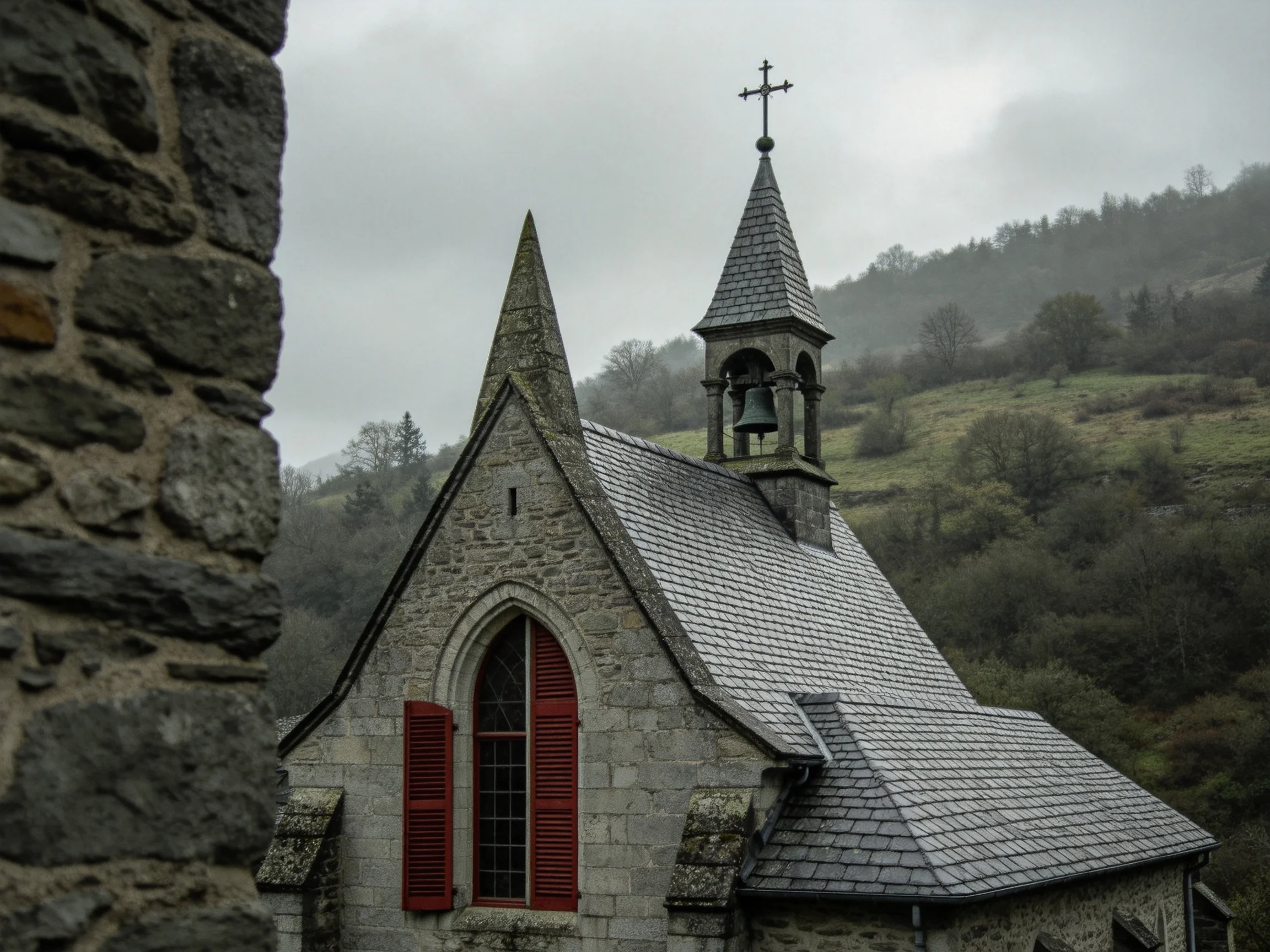 A stone church with red shutters, gray shingles, and a bell tower near green hills