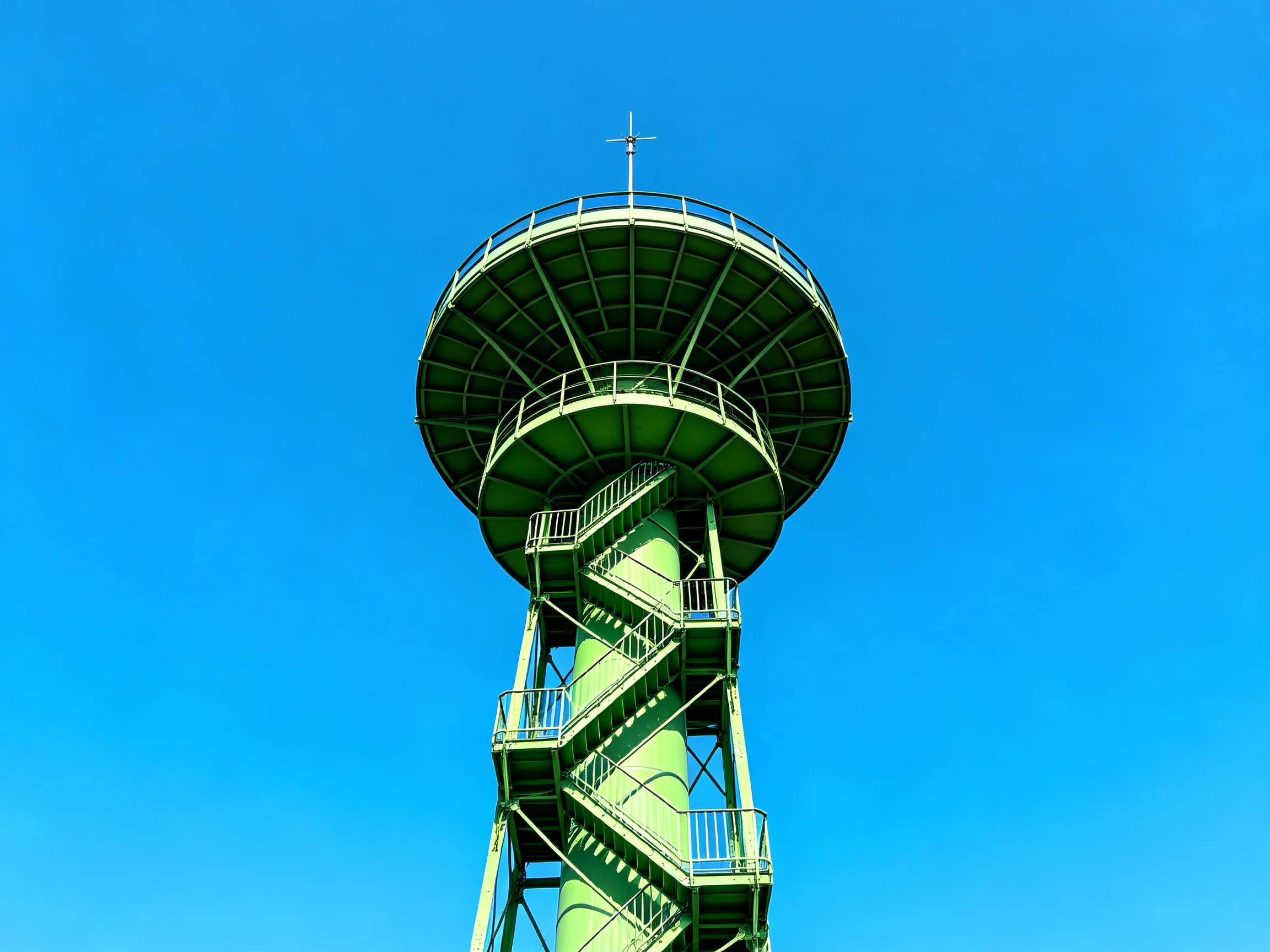 A tall green observation tower with spiral stairs under a clear blue sky