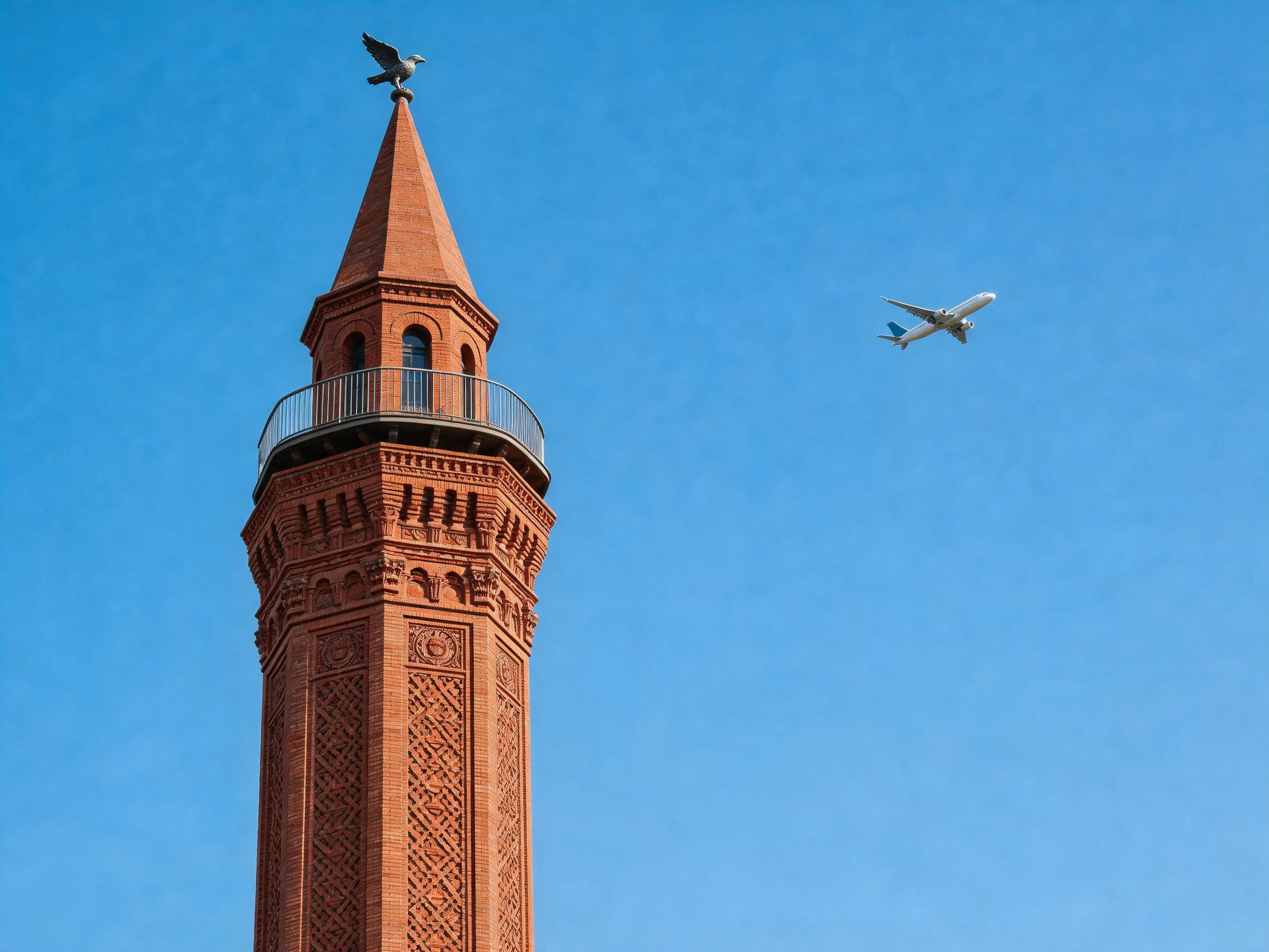 A tall reddish-brick tower with ornate details beside a jet under clear blue sky