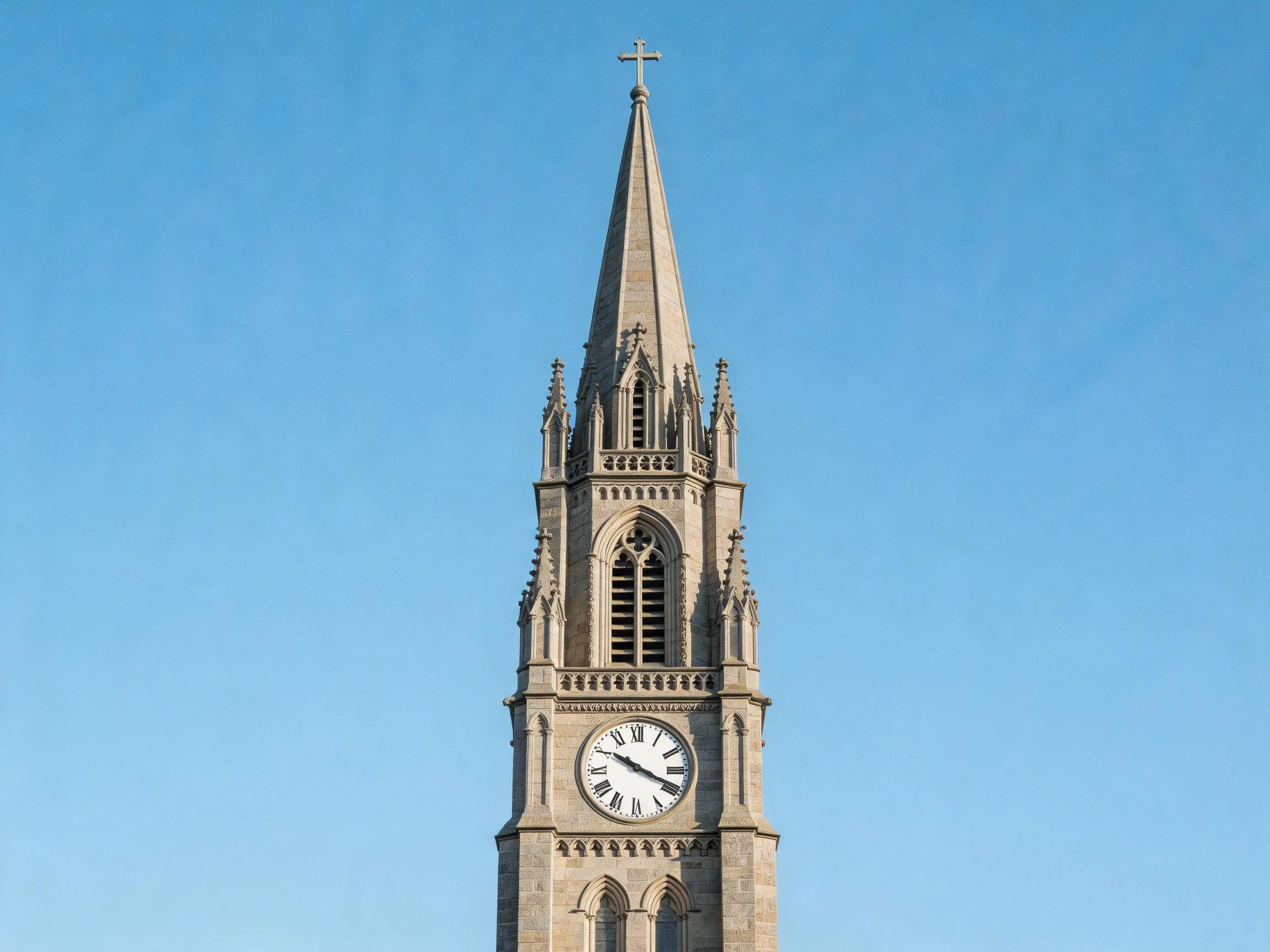 A tall stone clock tower with a clock face and pointed spire against clear blue sky