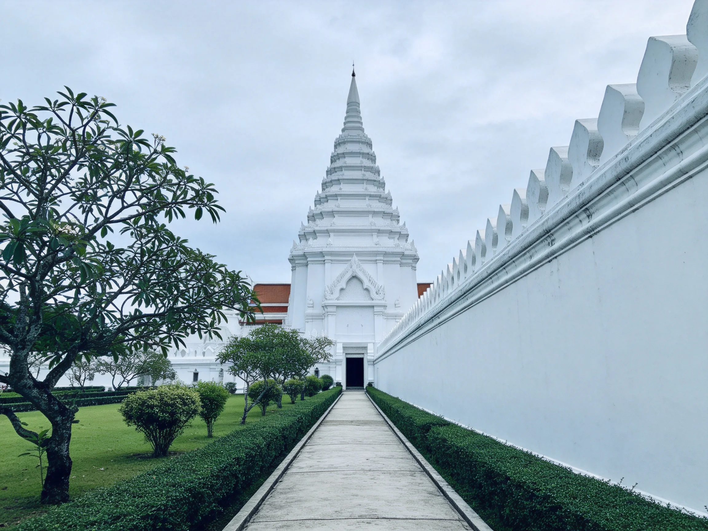 A tall white pagoda near a long stone pathway with manicured greenery