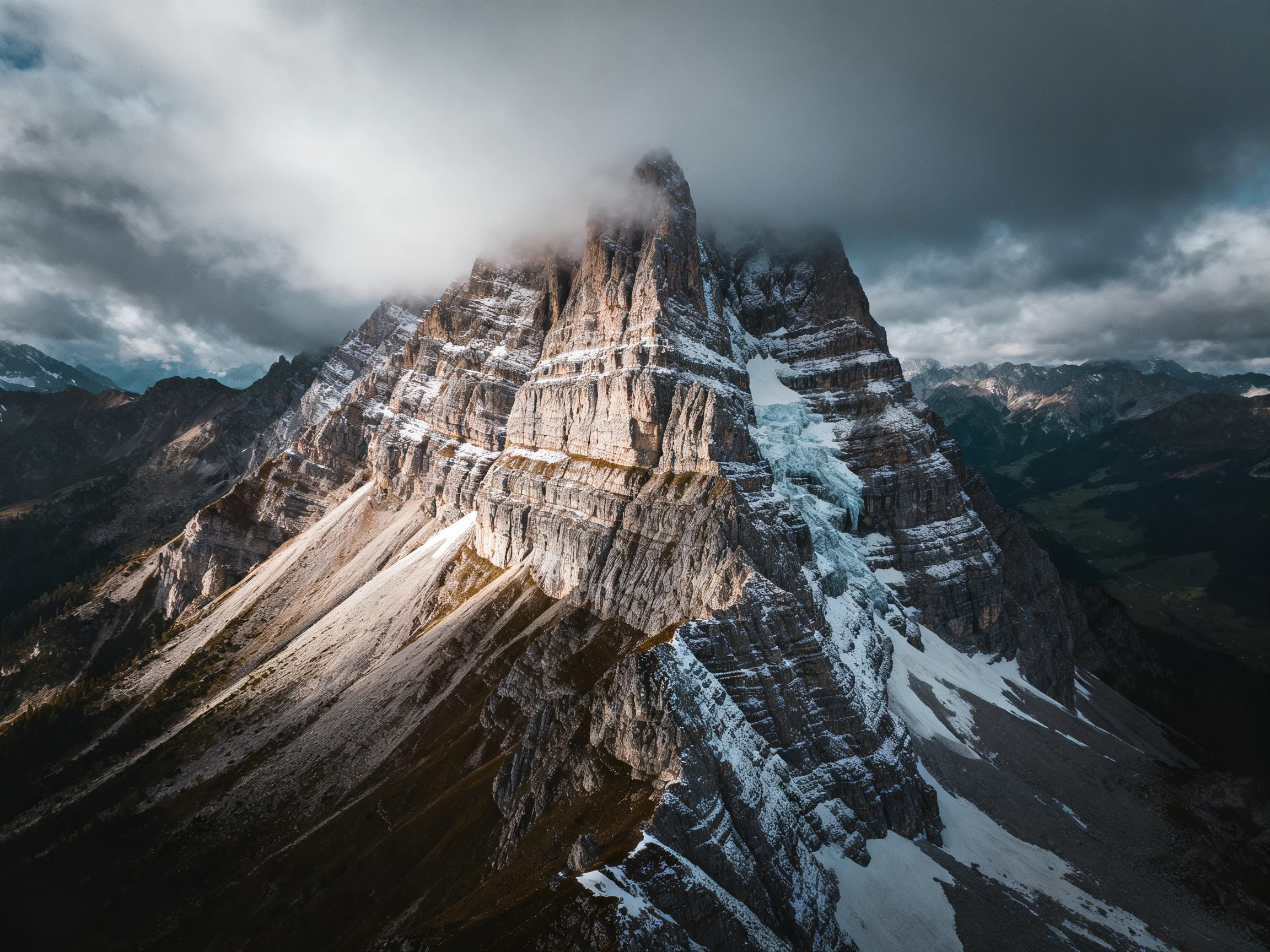 A towering rocky mountain peak with snow streaks and stormy clouds